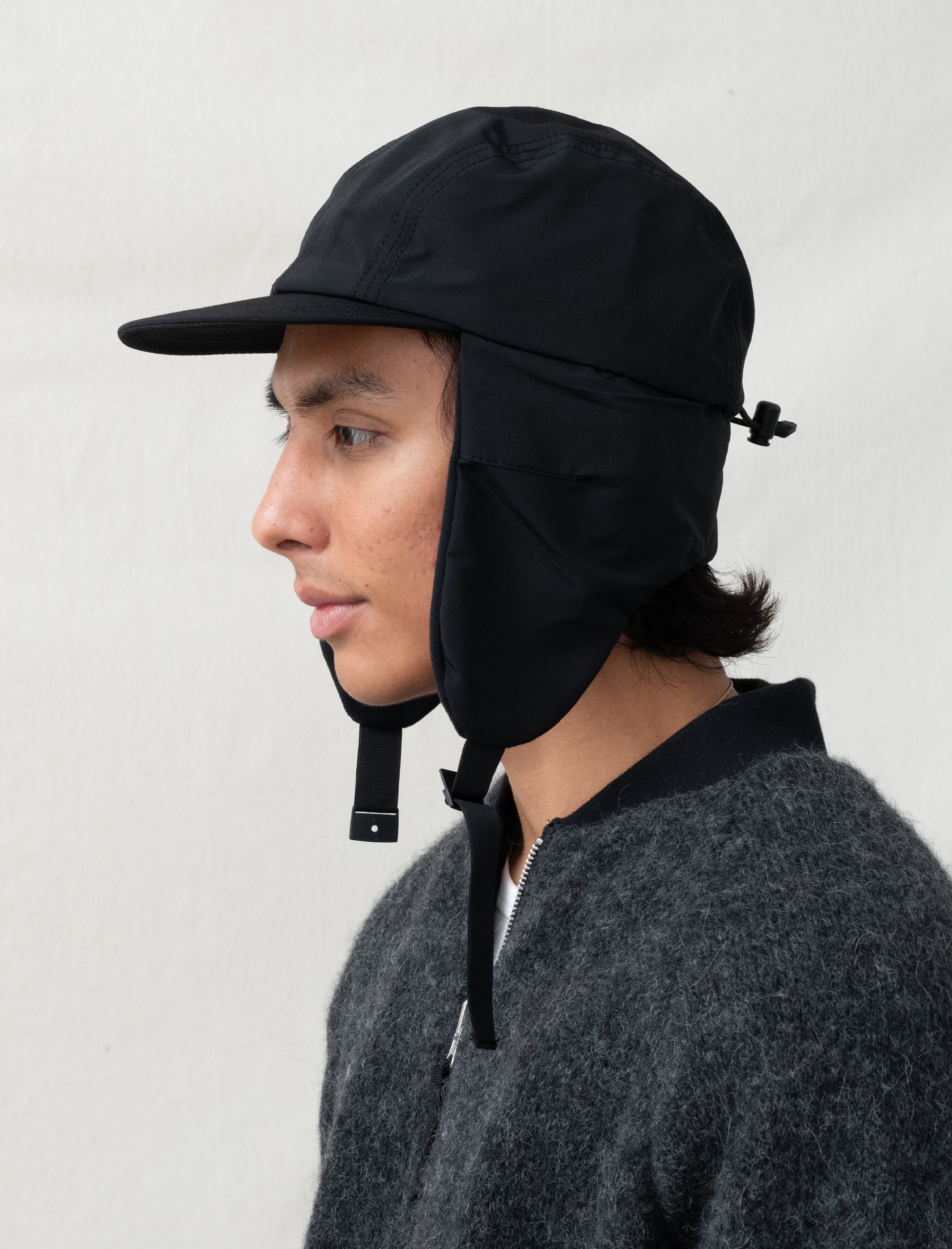 Person wearing a black cap with a neck cover against a white background