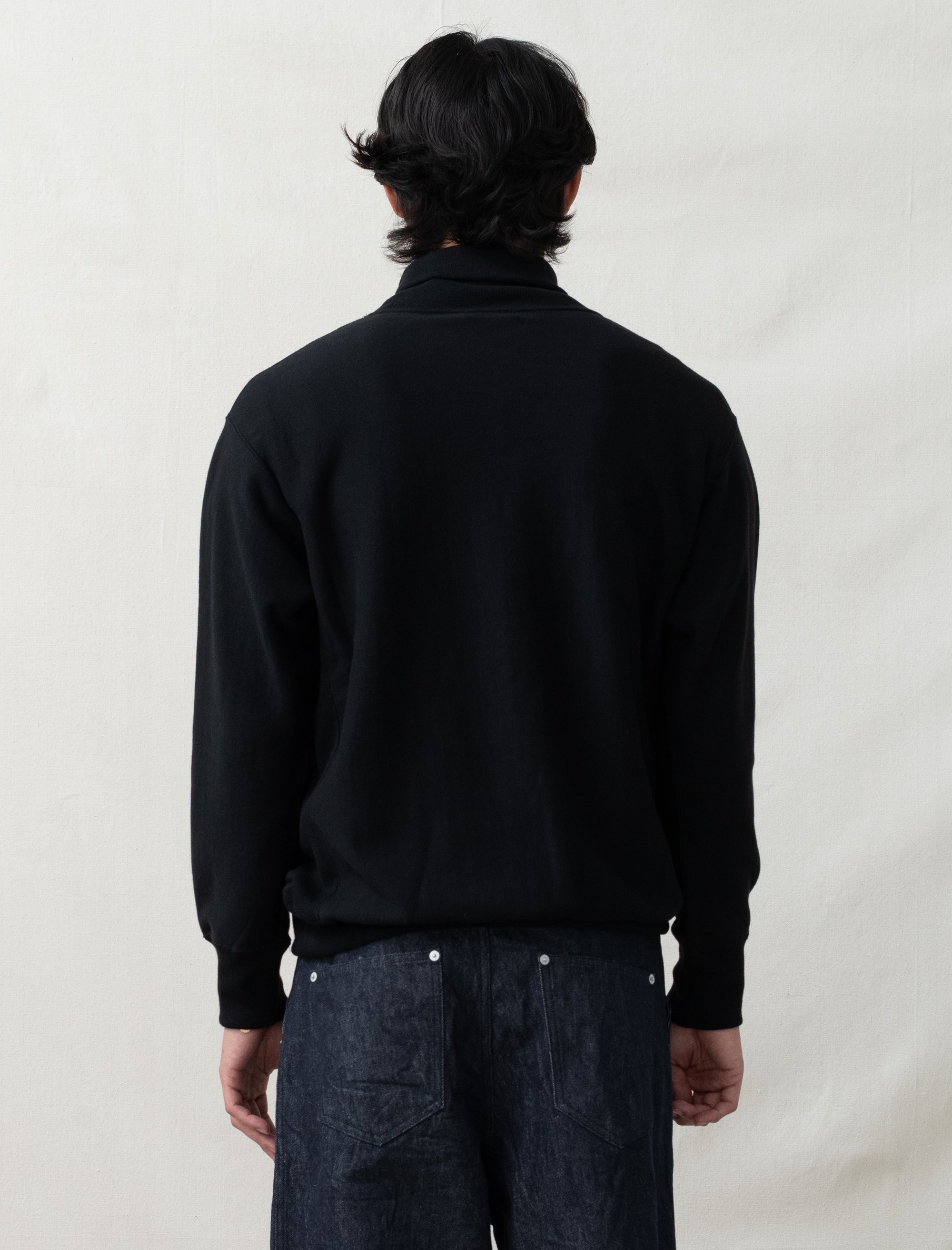 Person wearing a black jacket and dark jeans on a plain background