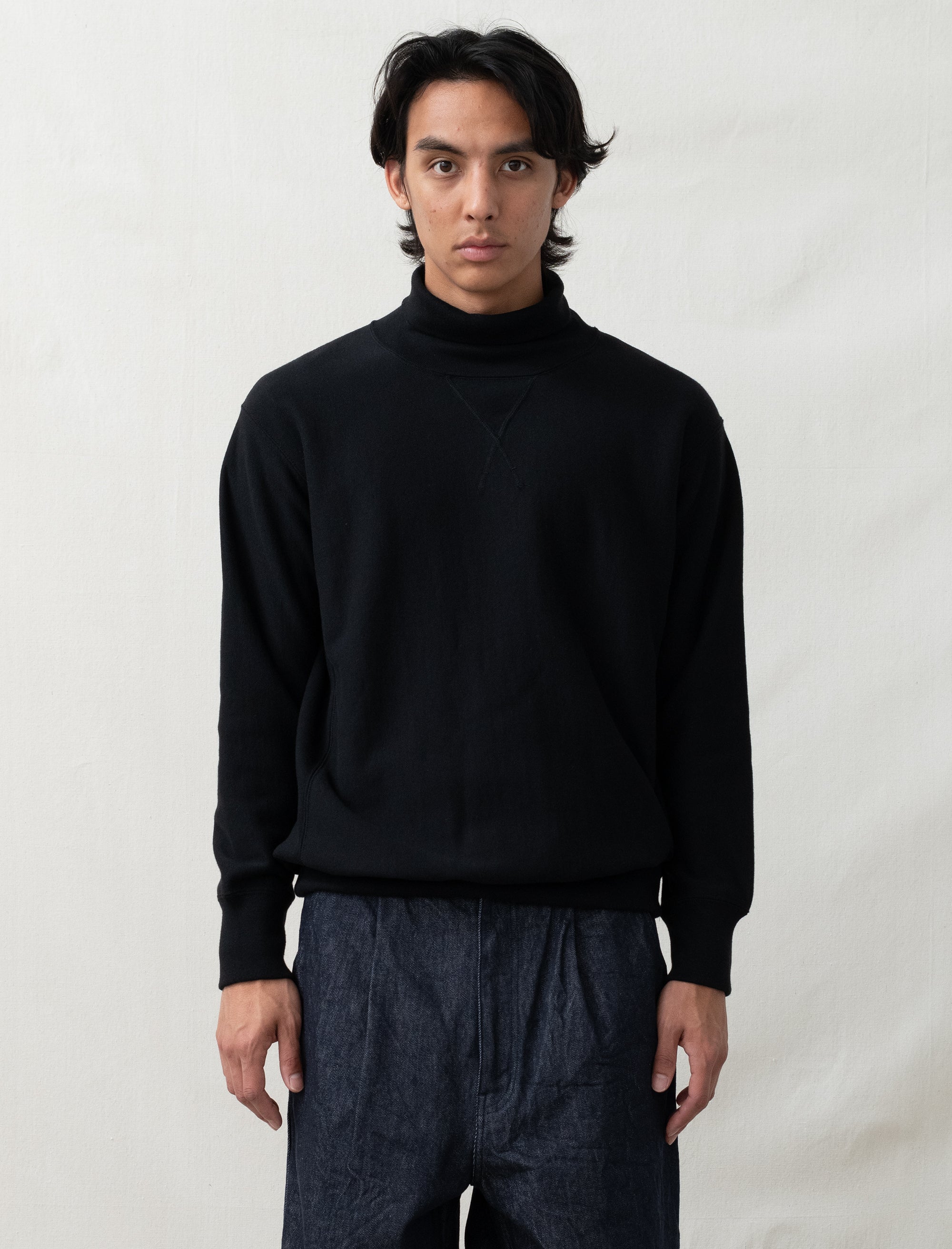 Person wearing a black turtleneck sweater and dark pants against a white background