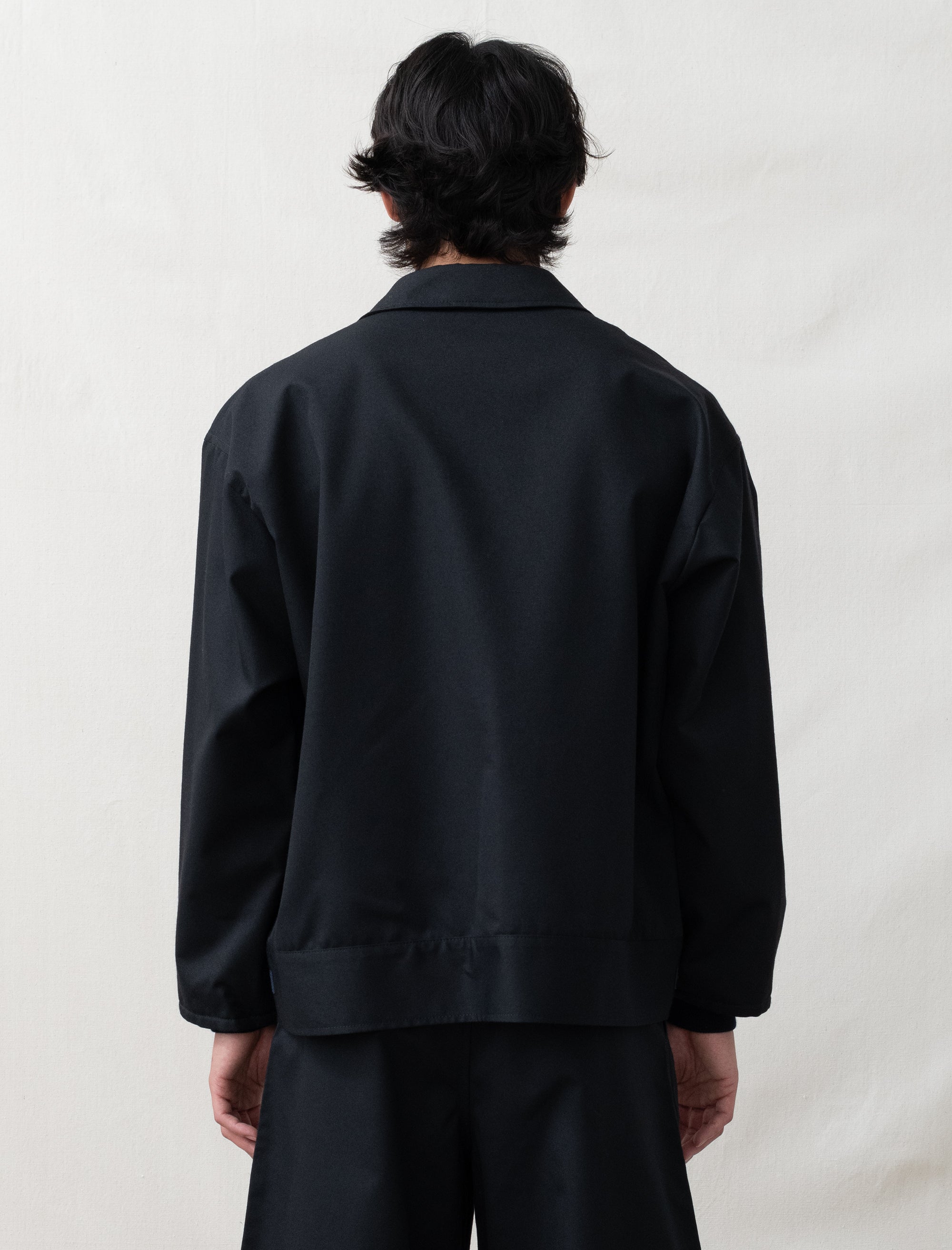 Person wearing a black jacket and pants against a plain background