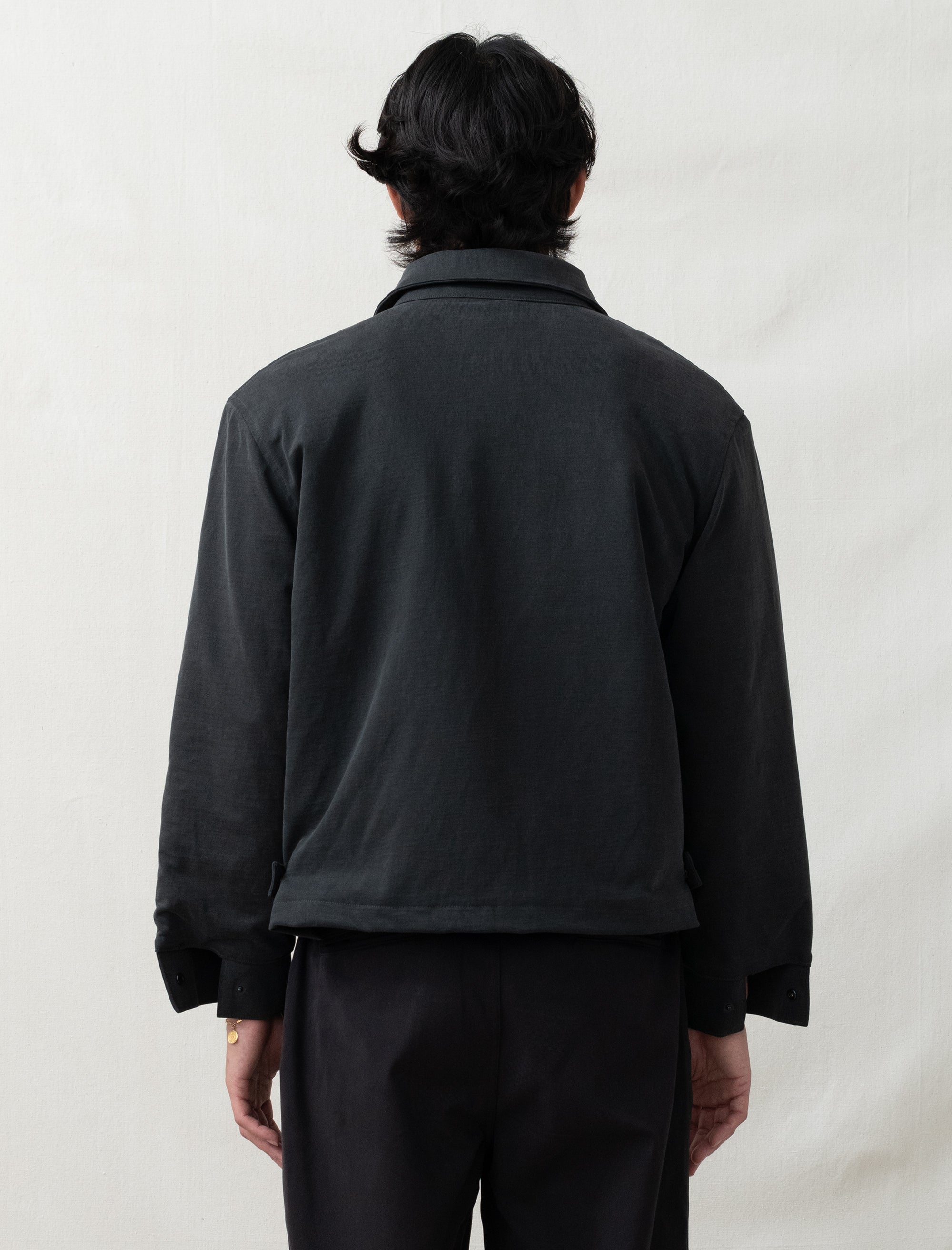 Person wearing a black jacket and pants against a plain background