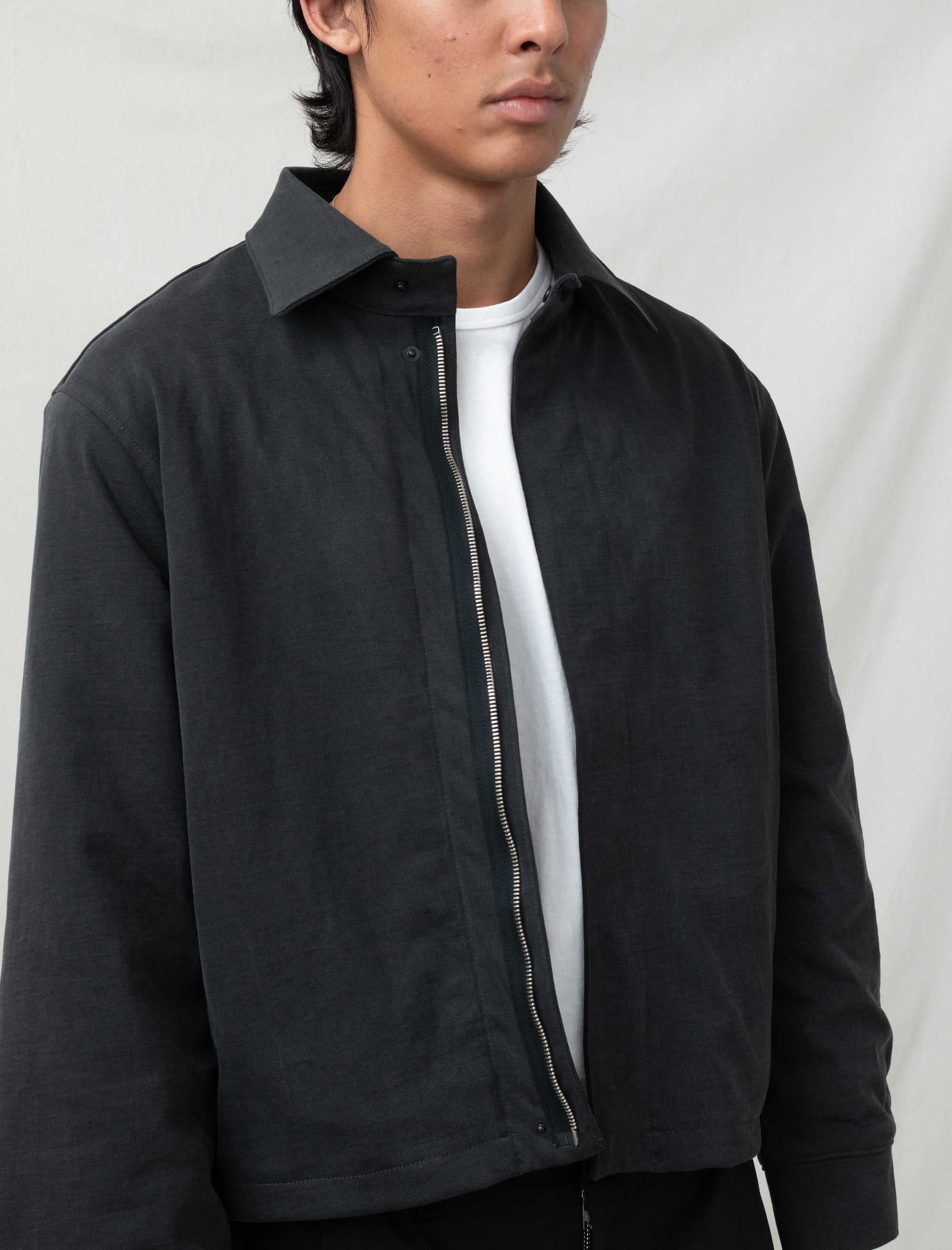 Person wearing a black jacket over a white shirt on a plain background