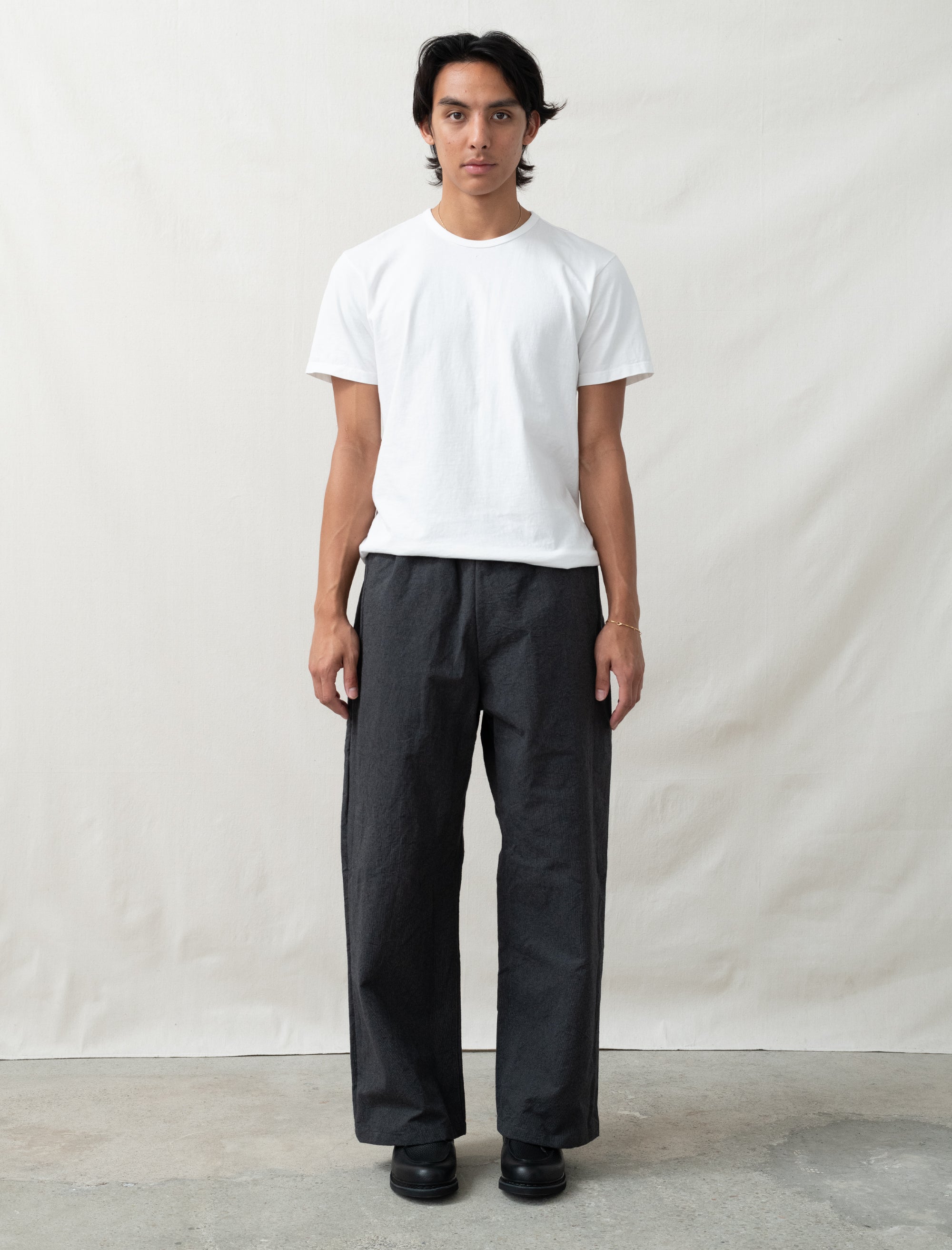 Person wearing a white t-shirt and black pants against a plain background