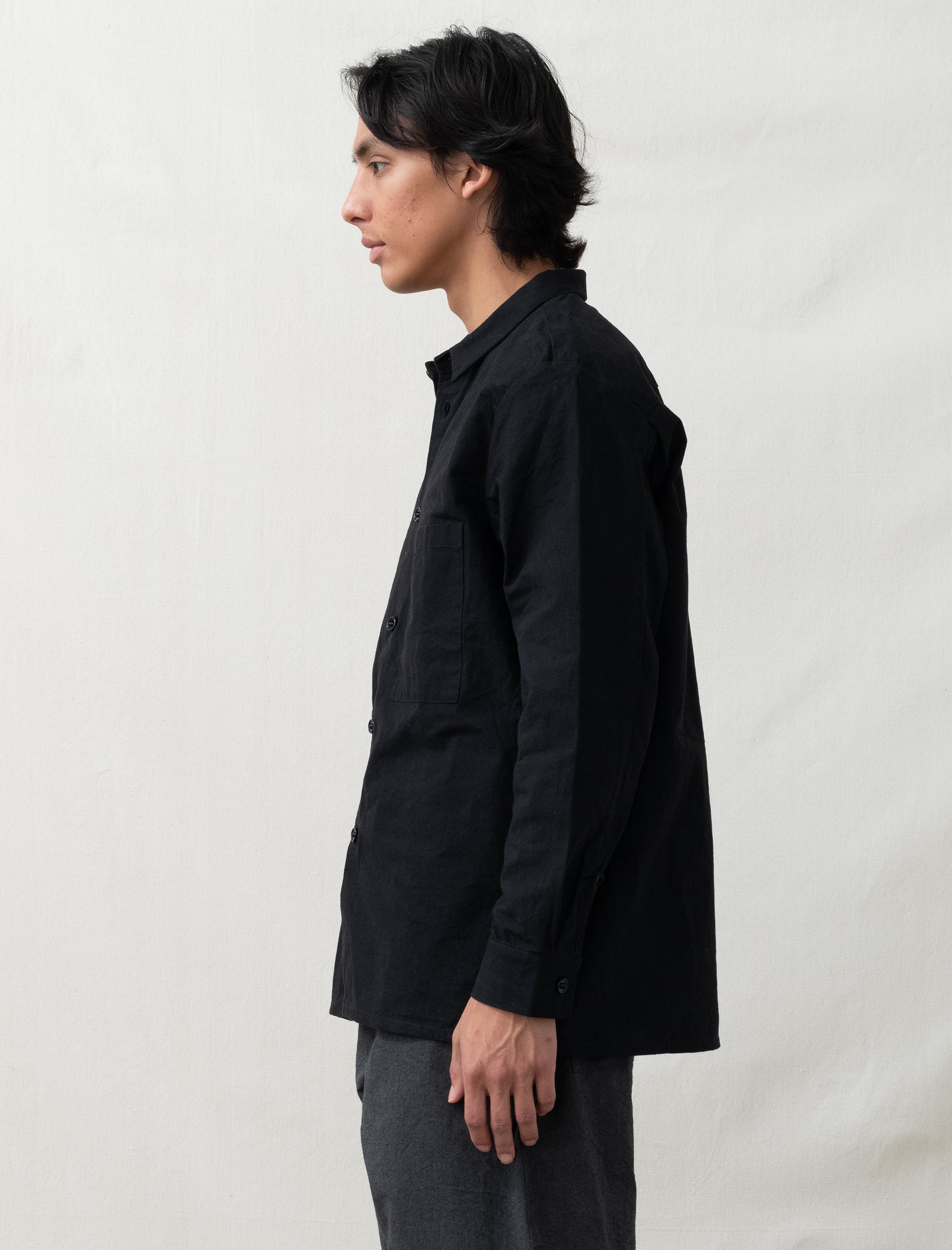 Person wearing a black jacket and gray pants standing against a plain white background