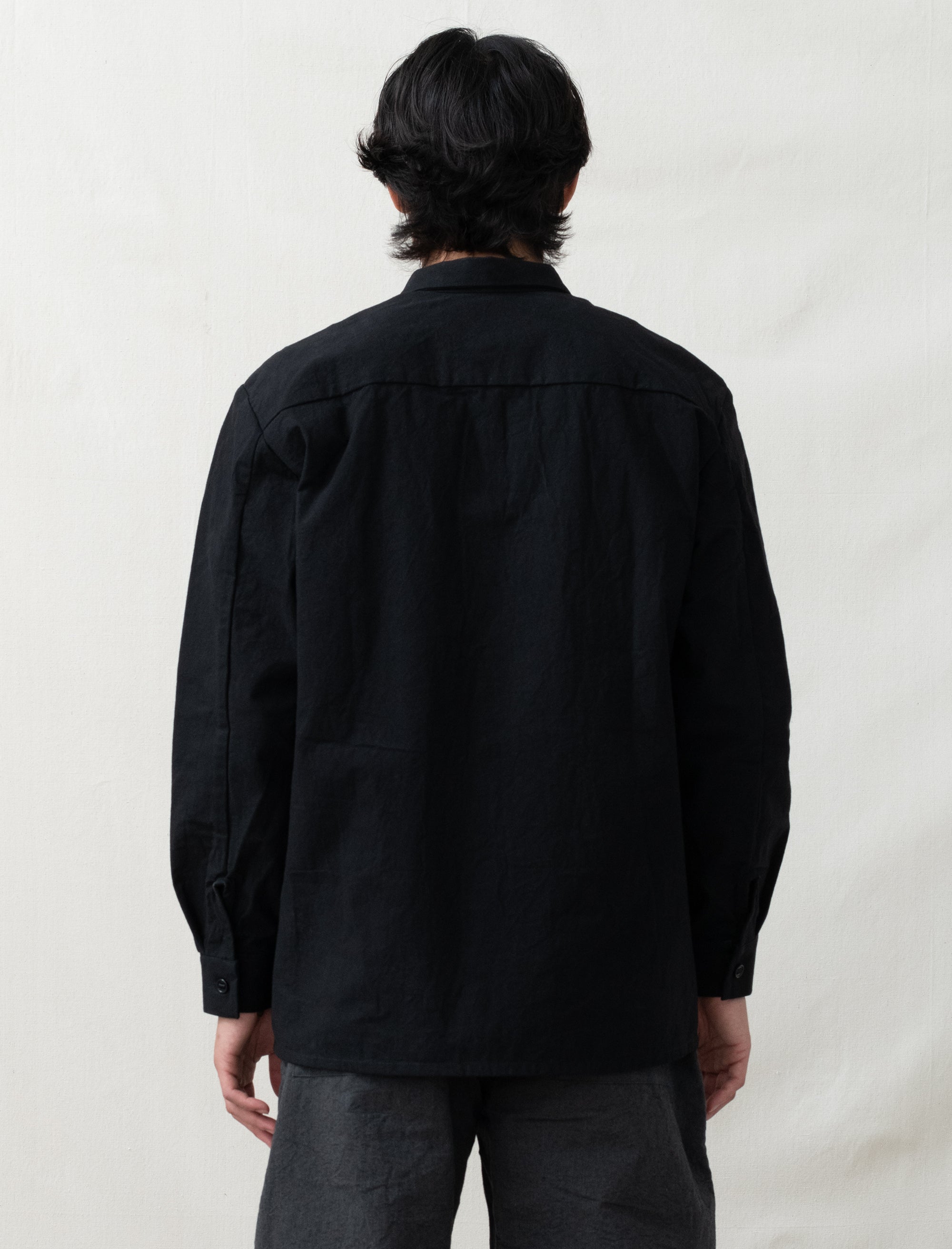 Person wearing a black jacket and gray pants standing against a plain white background