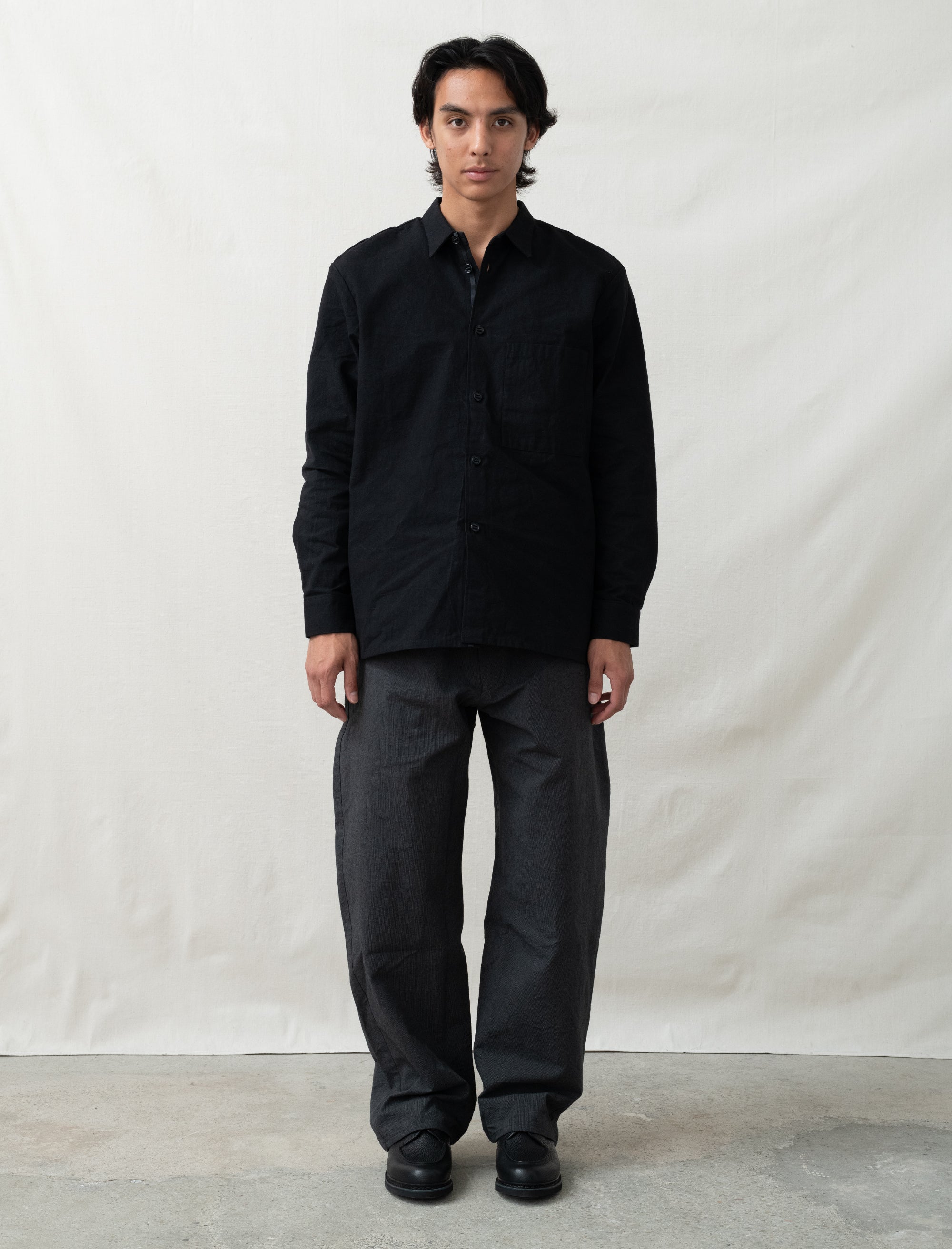 Person wearing a black shirt and dark pants against a plain background