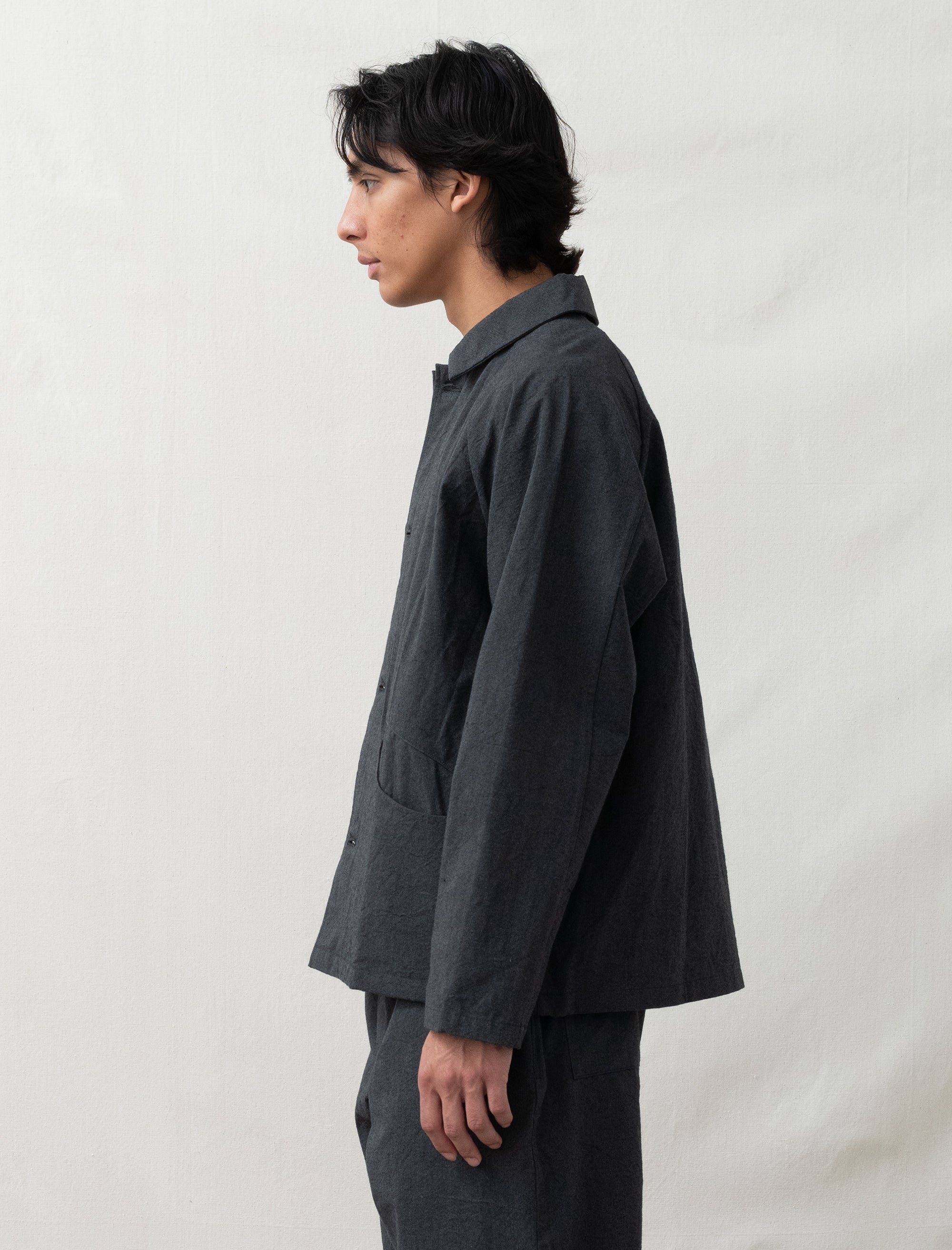 Person wearing a dark gray jacket and pants against a plain background