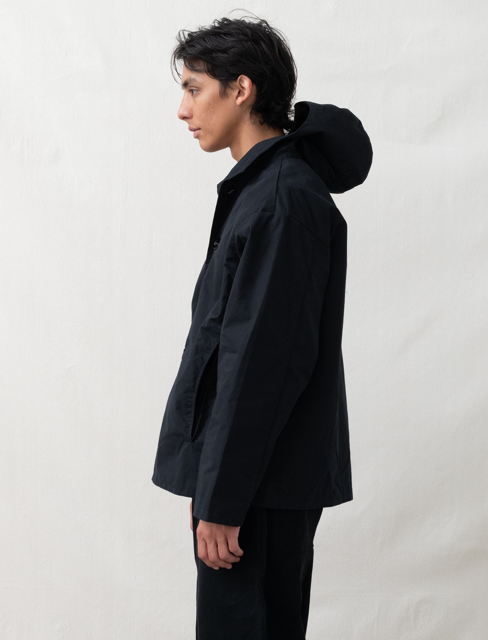 Person wearing a black jacket with a hood against a plain background