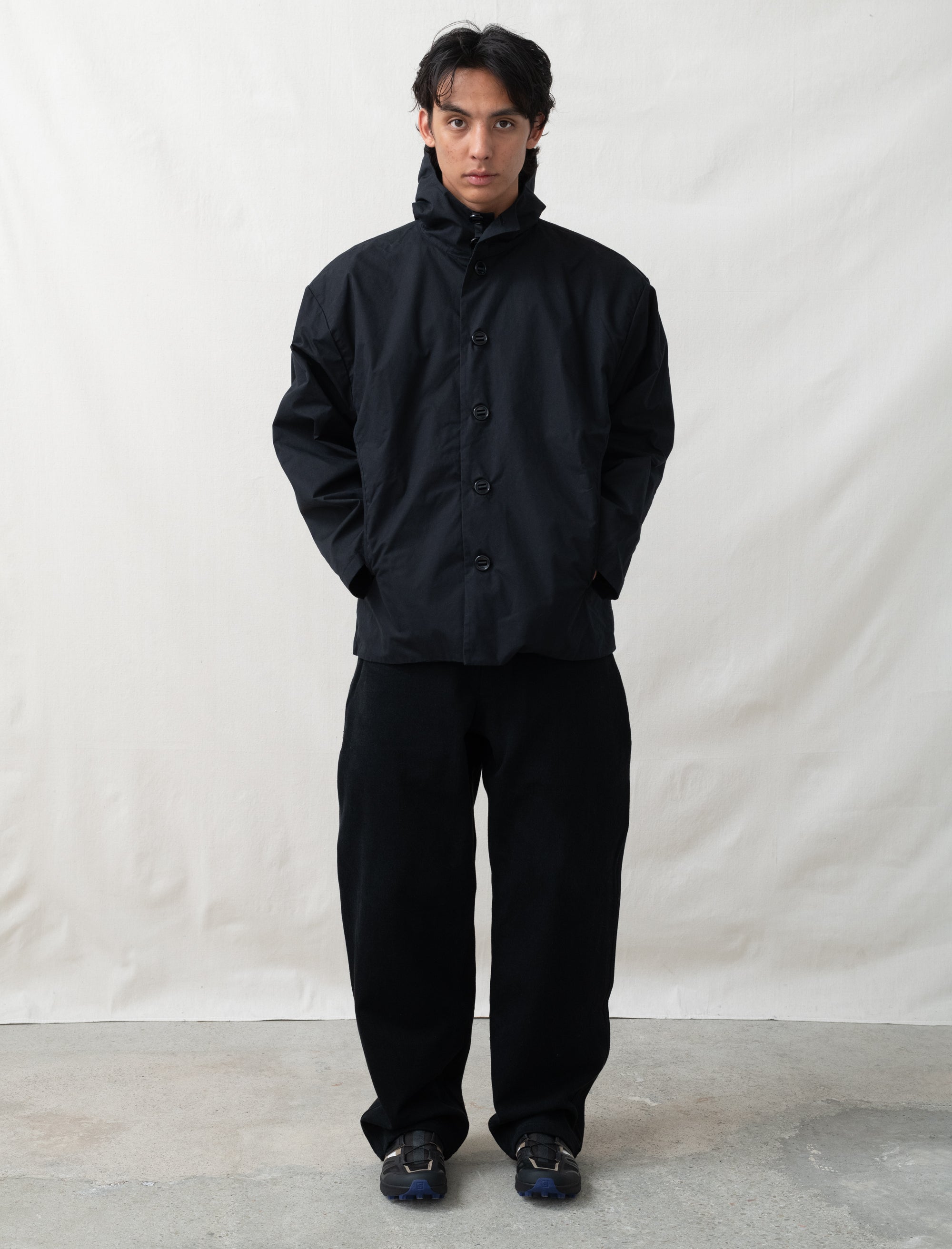 Person wearing a black raincoat and pants against a white background