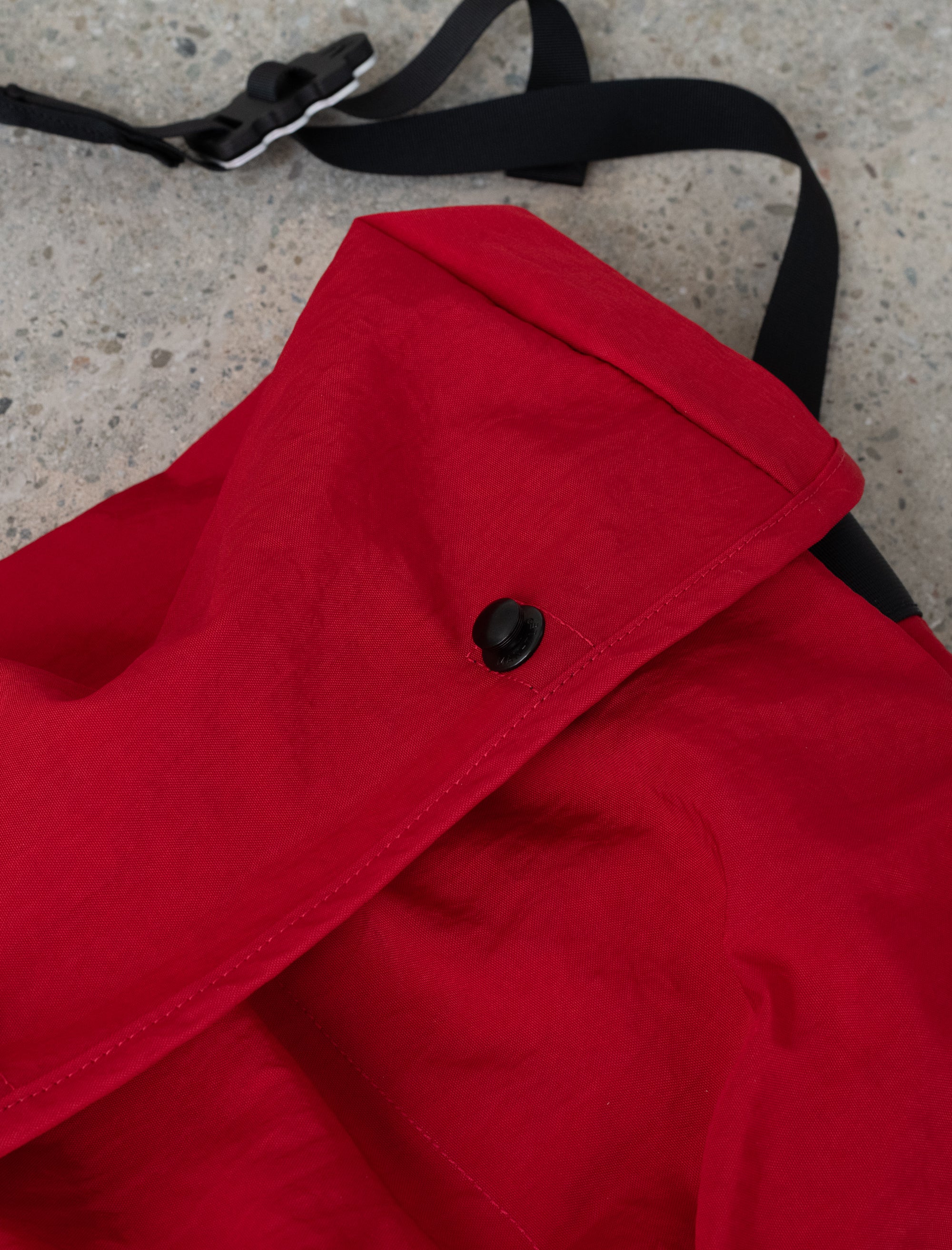 Red coat with a black strap on a concrete surface