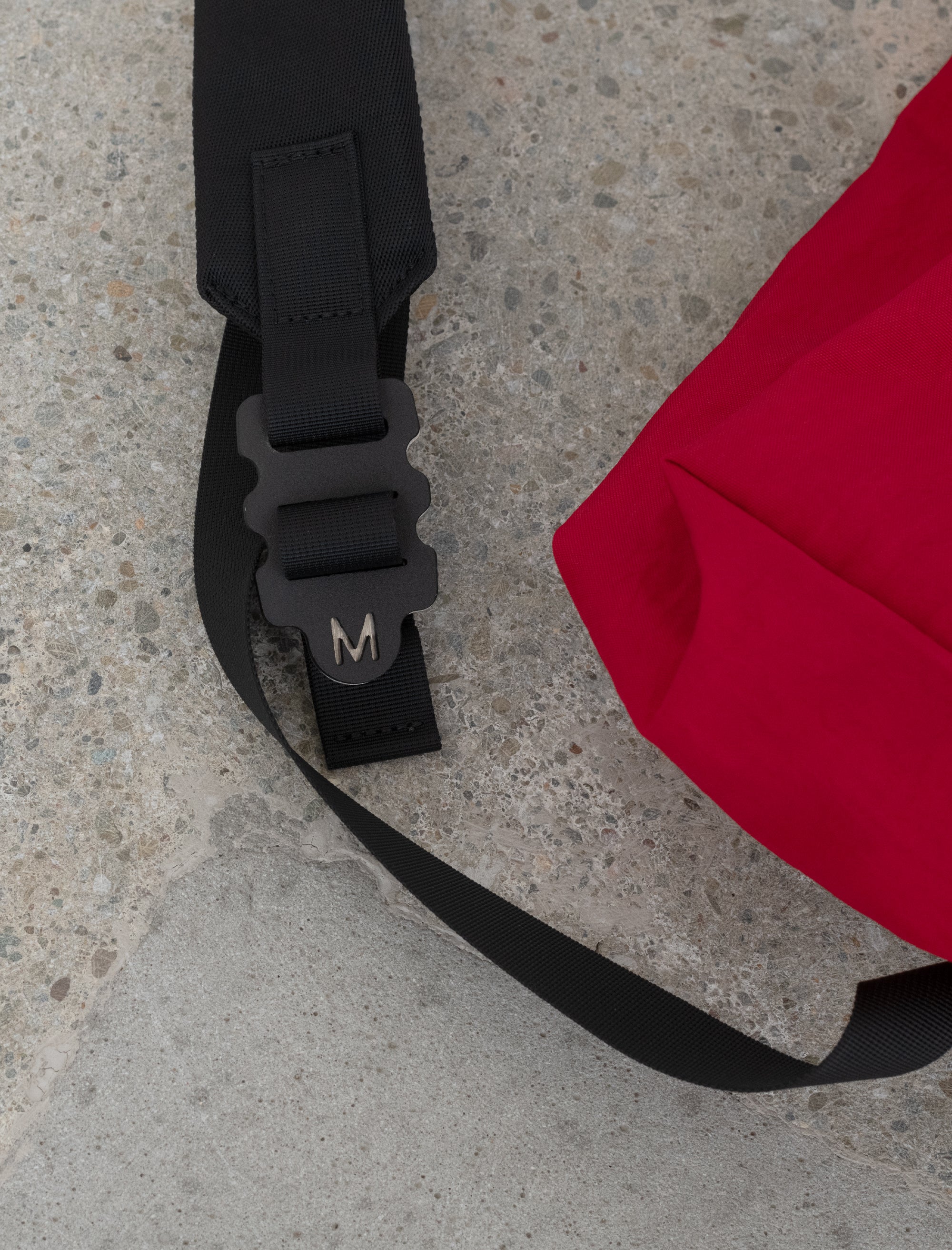 Black strap with a logo on a red bag against a concrete floor background