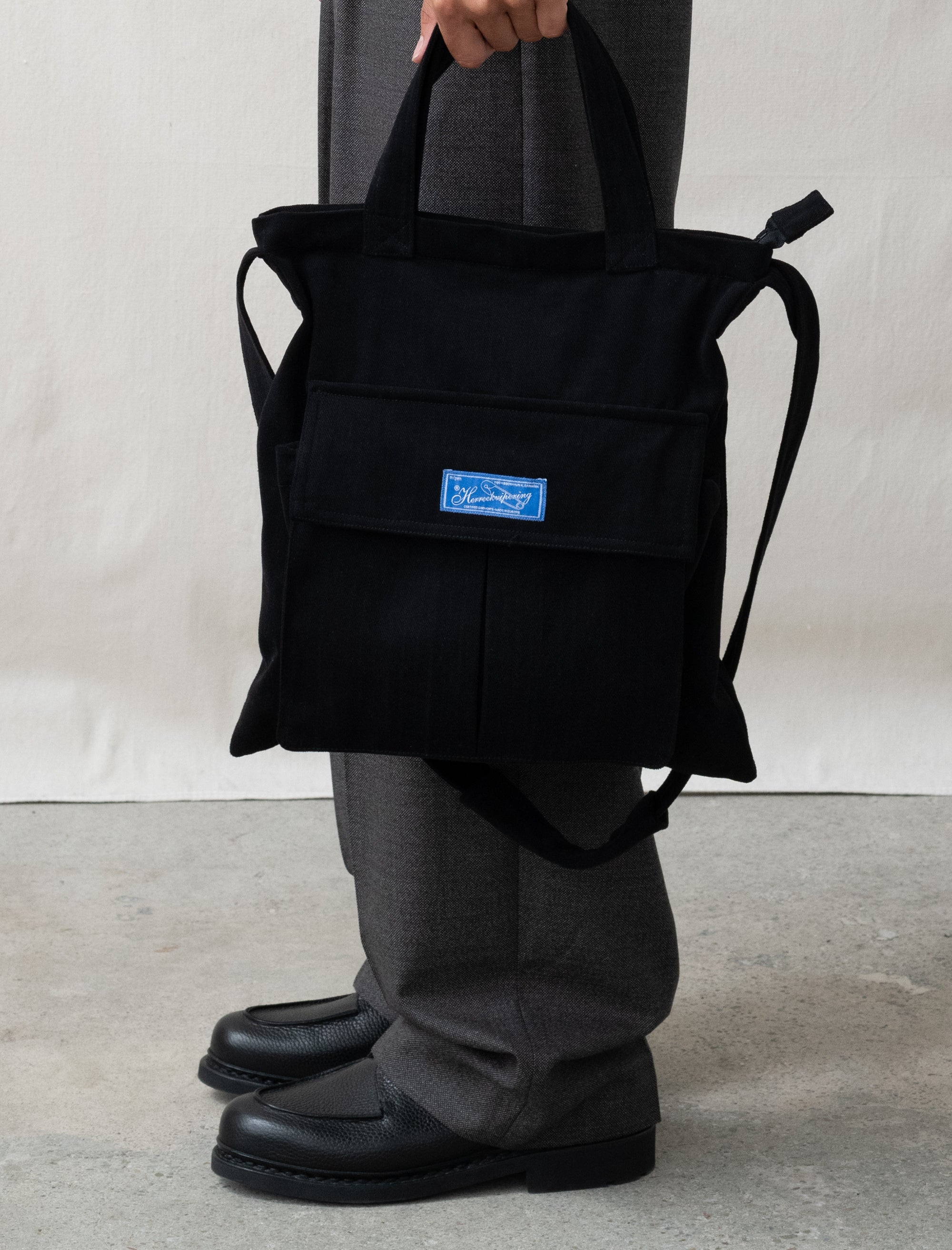 Person holding a black backpack with a blue label on a neutral background
