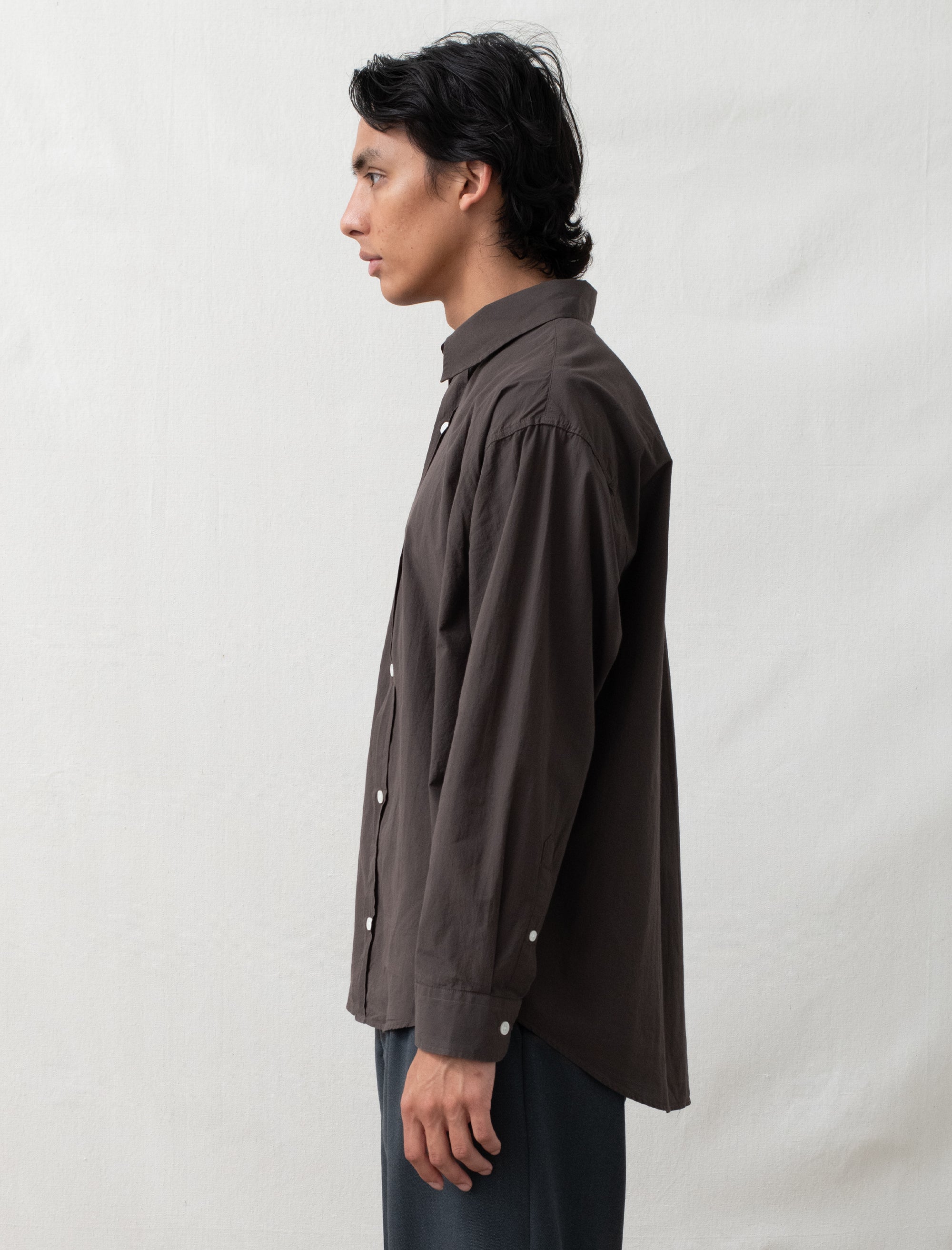 Person wearing a dark brown shirt with white buttons against a plain background