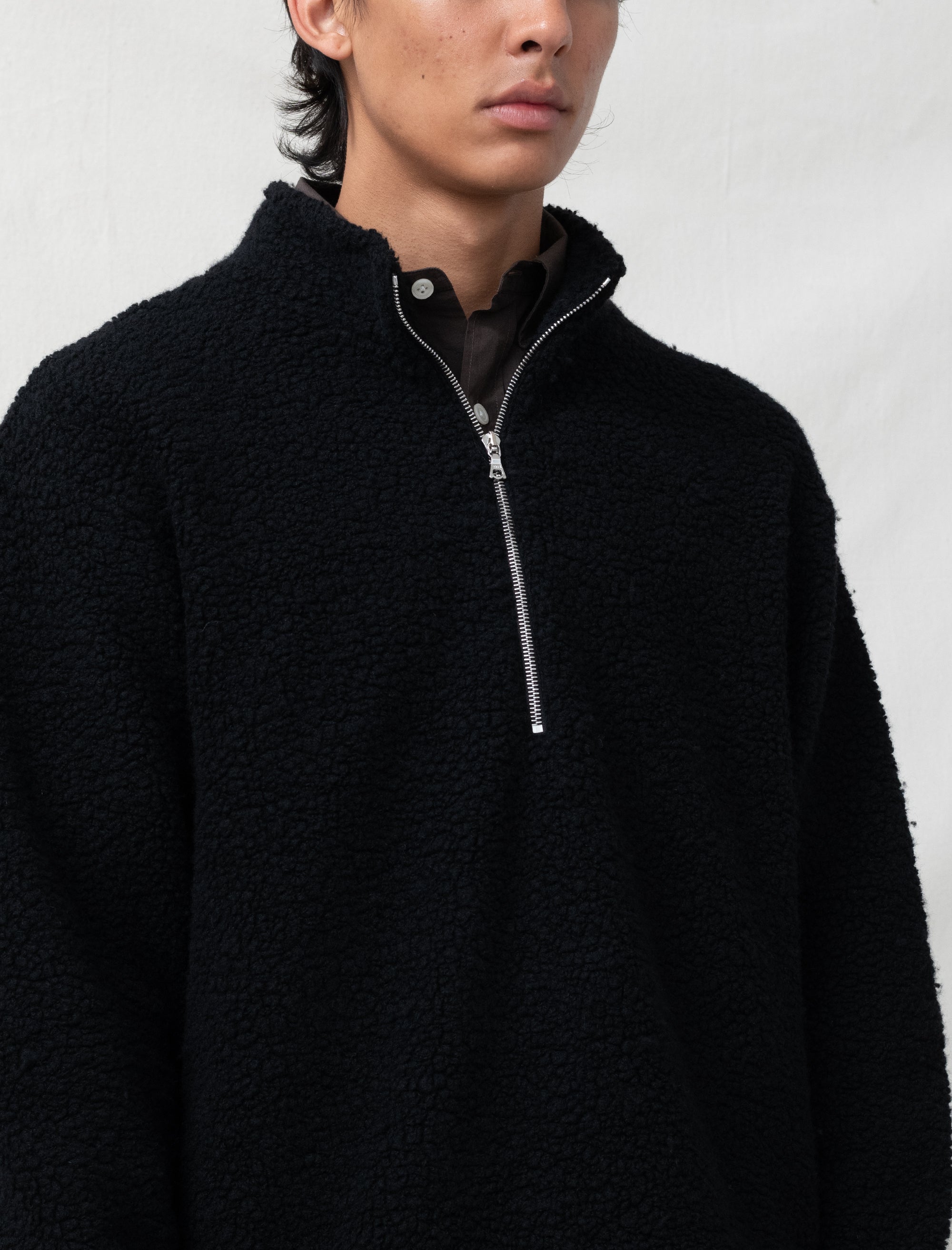 Person wearing a black fleece pullover with a zipper on a white background