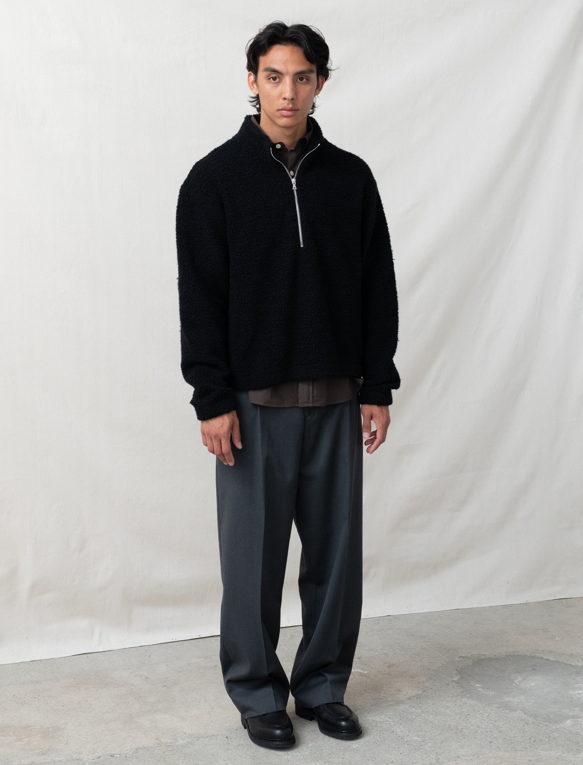 Man wearing a black jacket and gray pants against a white background