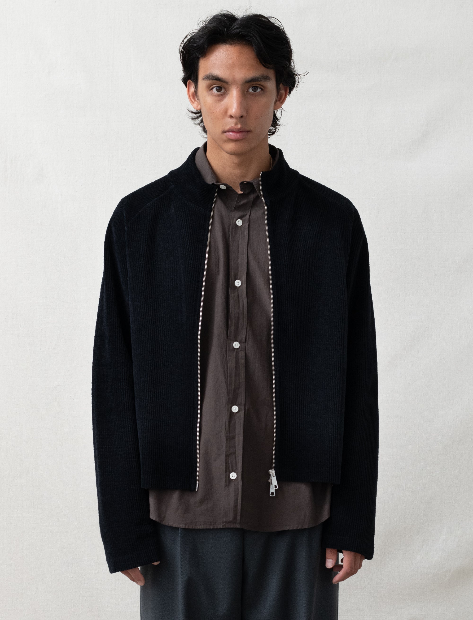 Man wearing a black jacket over a brown shirt on a white background