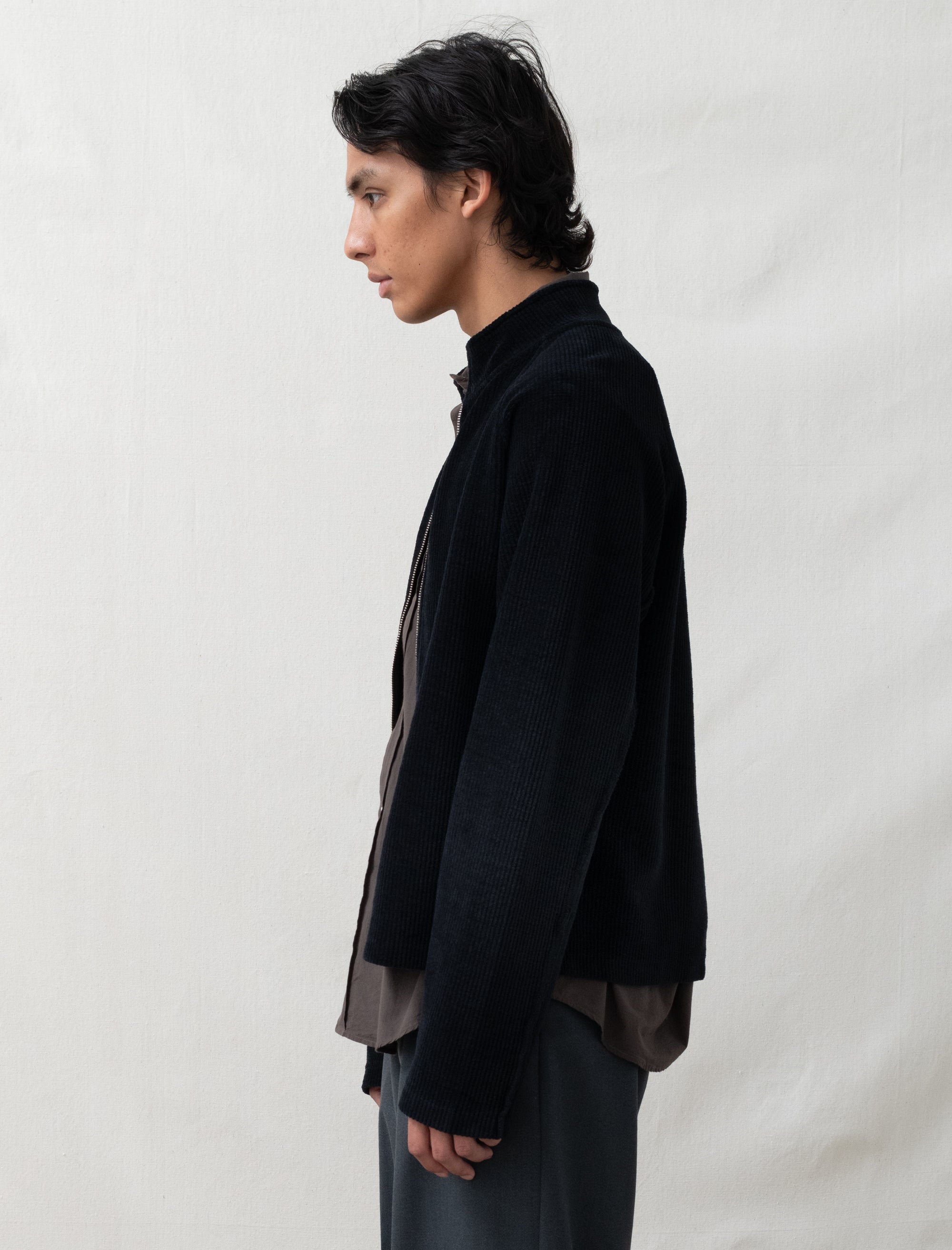 Person wearing a black jacket and dark pants against a plain background