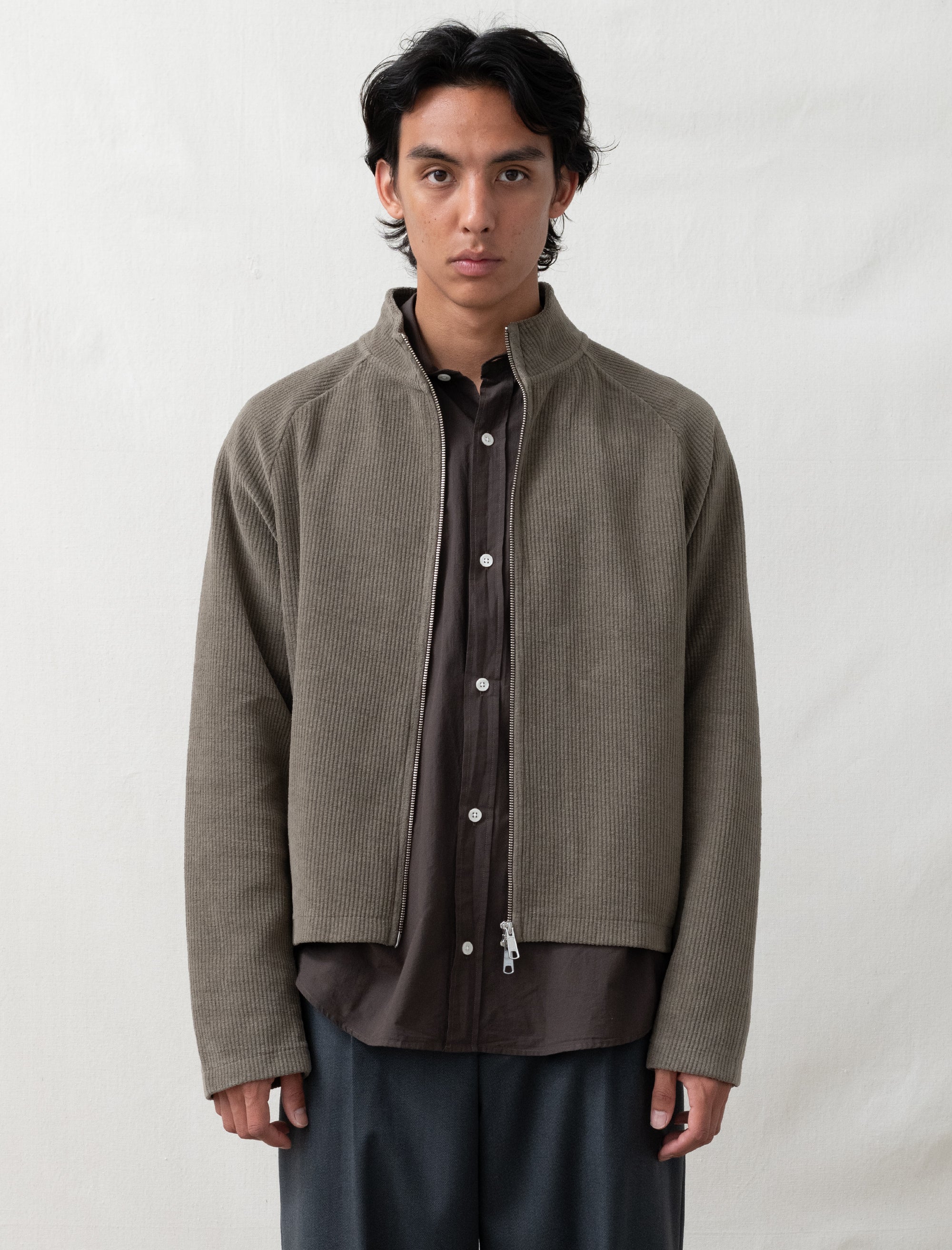 Man wearing a brown jacket over a dark shirt on a white background