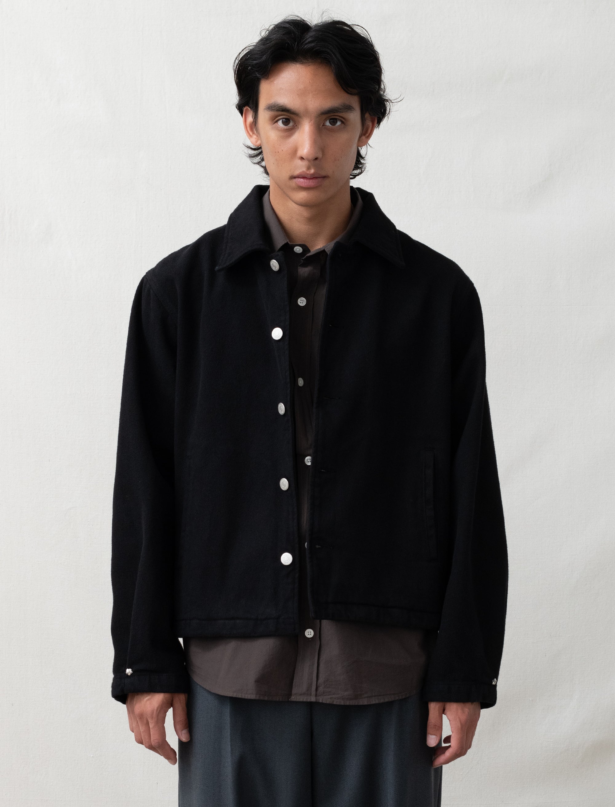 Person wearing a black jacket over a dark shirt on a white background