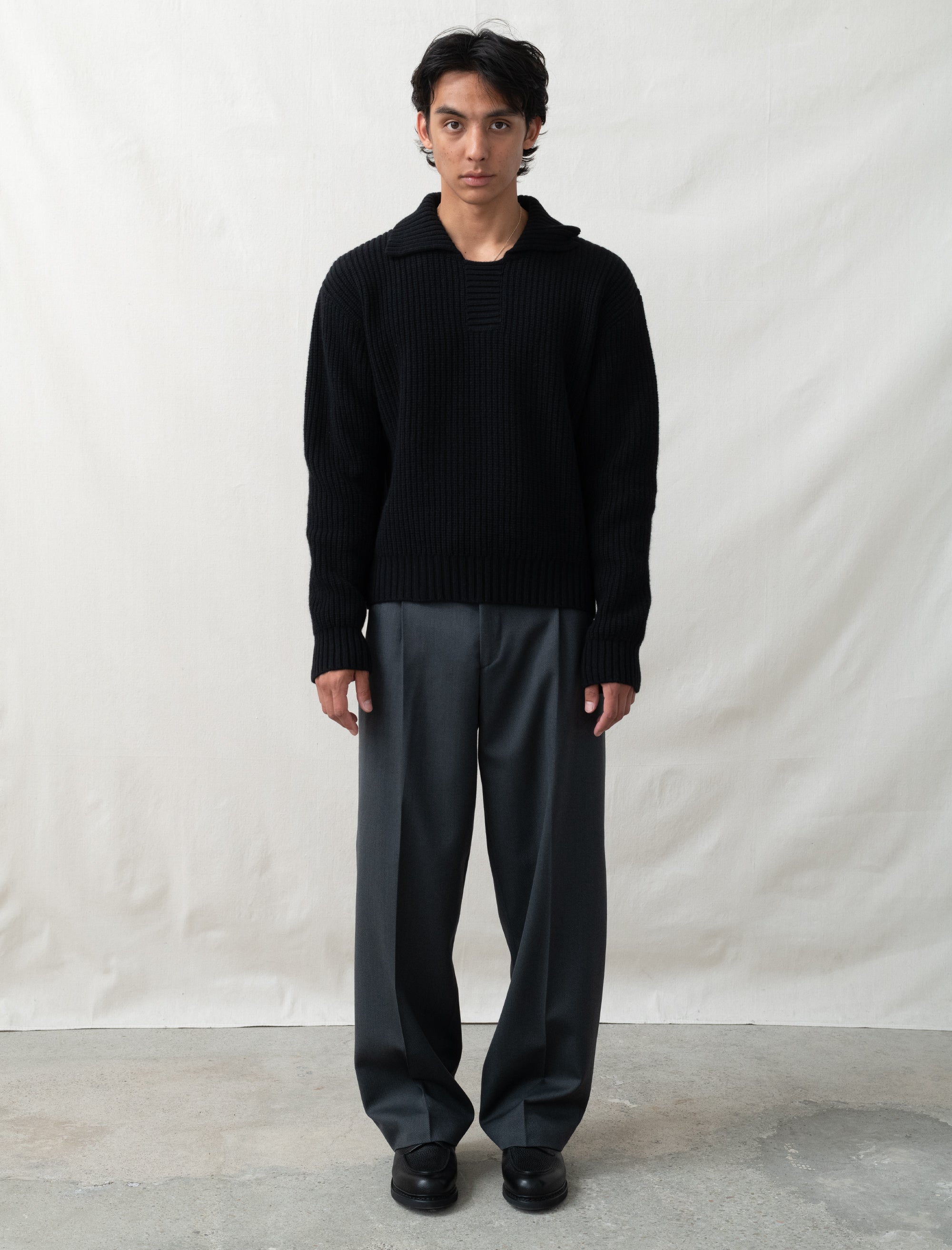 Person wearing a black sweater and gray pants against a plain background