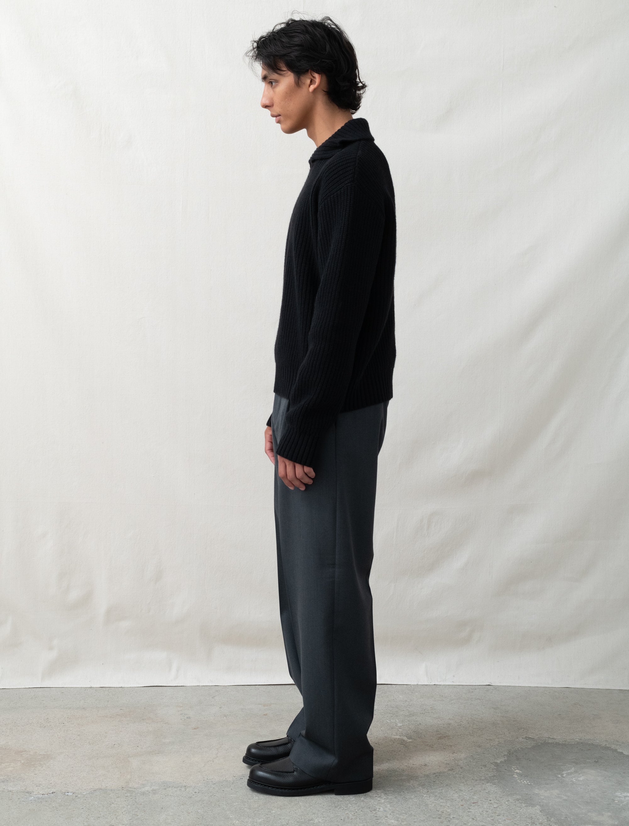 Person wearing a black shirt and gray pants against a plain white background