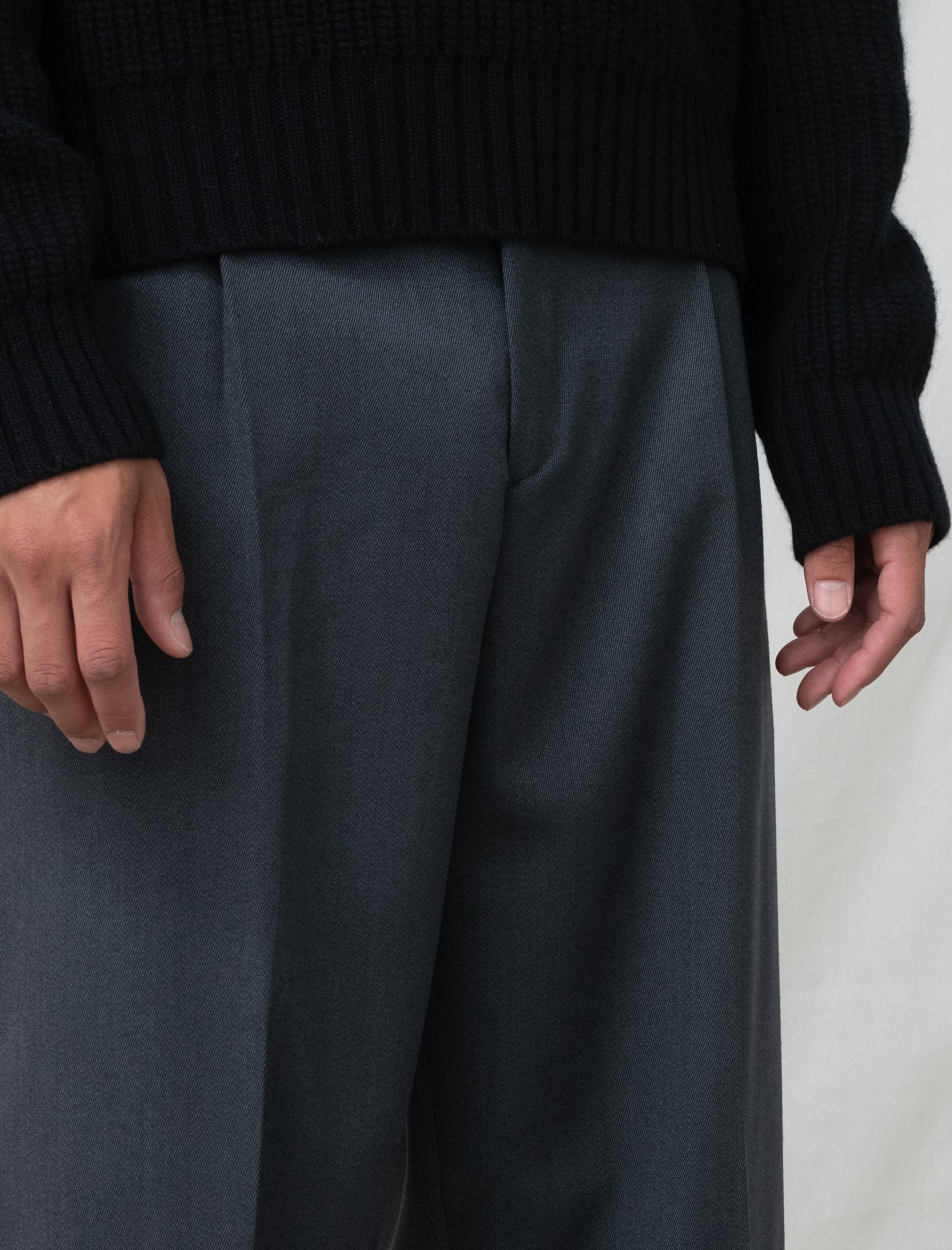 Person wearing dark gray wide-leg pants and a black sweater against a neutral background