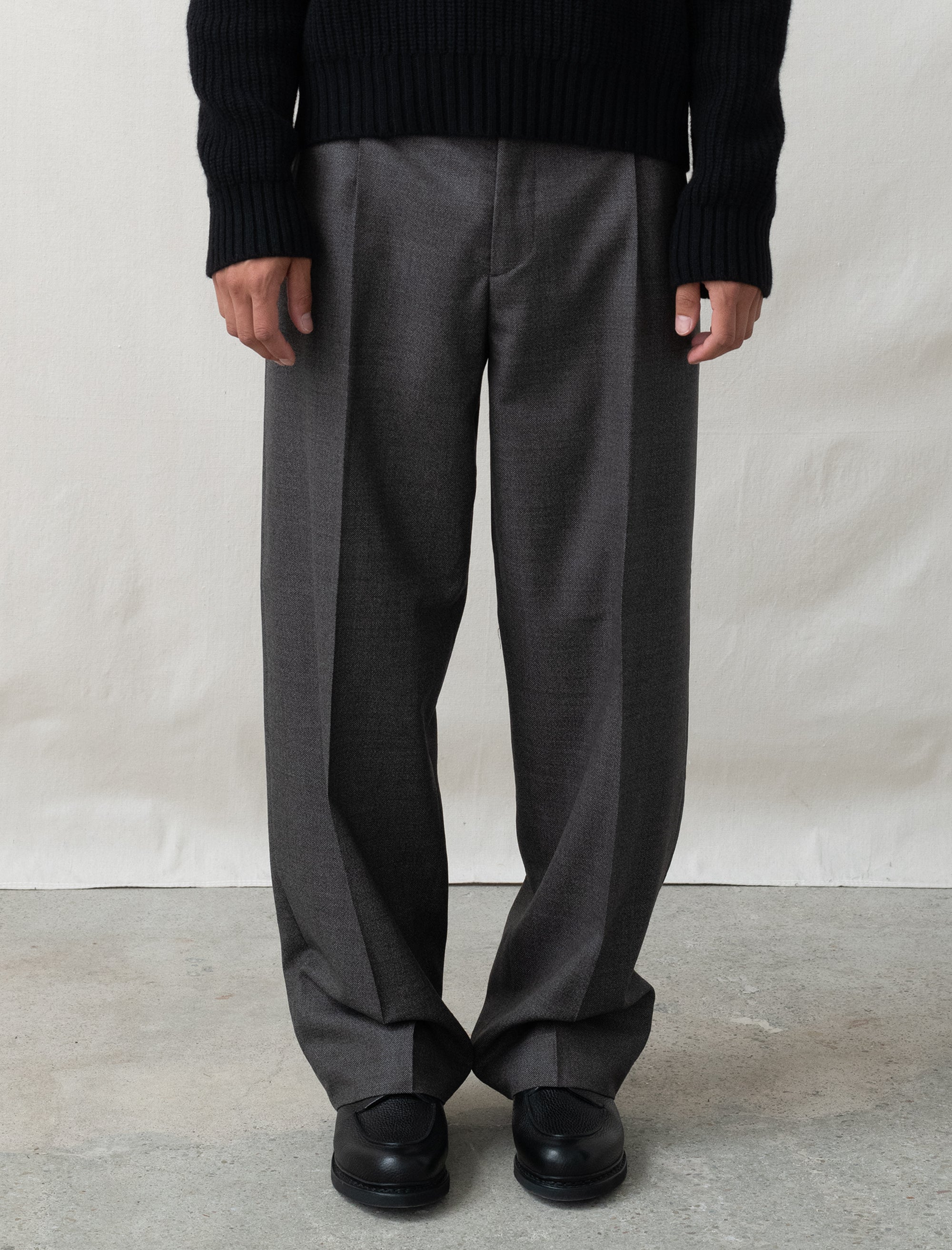 Person wearing gray wide-leg pants and black shoes on a plain background