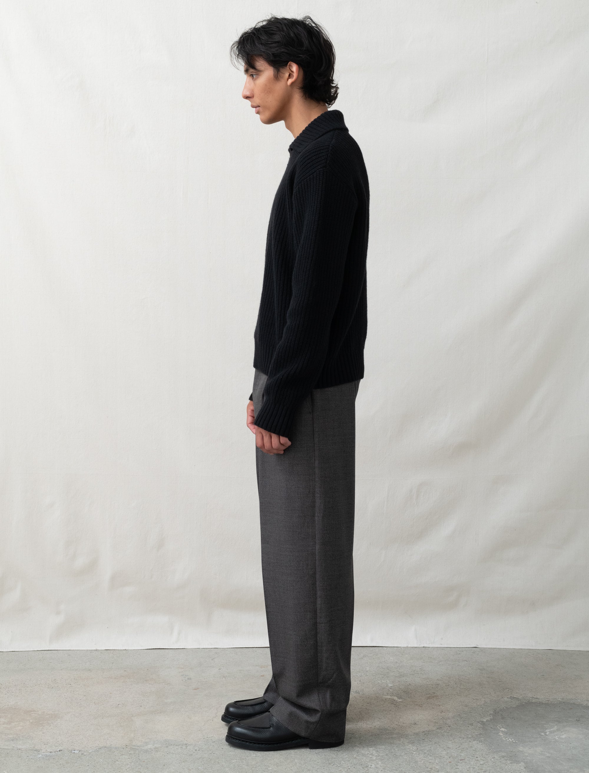 Person wearing a black shirt and gray pants standing against a plain white background