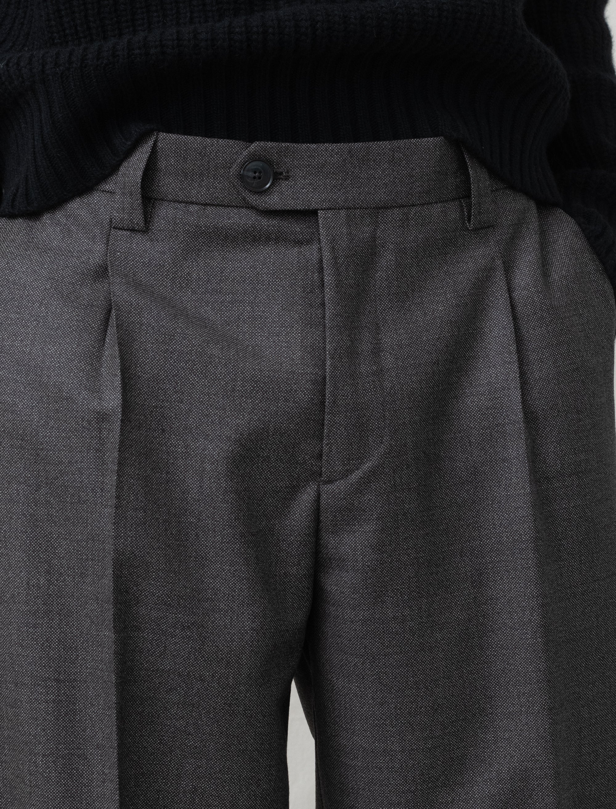 Close-up of gray pleated pants with a button on a plain background
