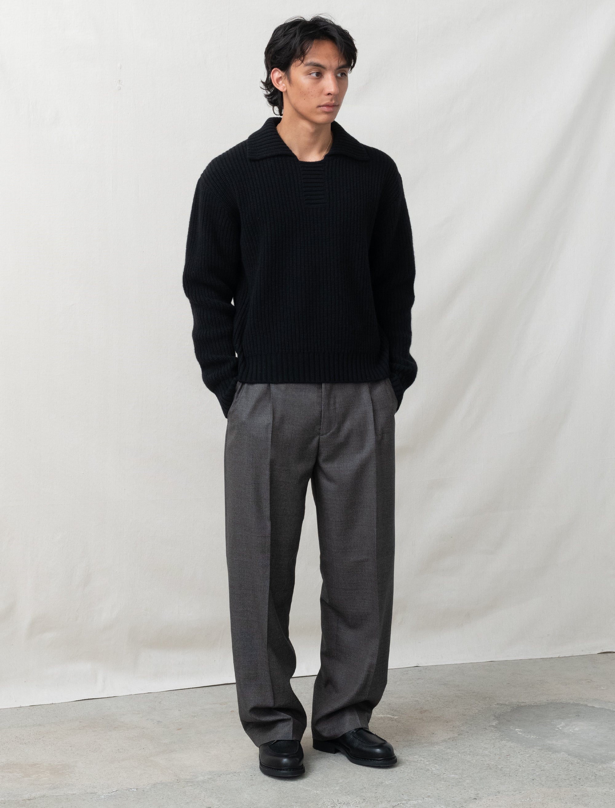 Person wearing a black sweater and gray pants against a plain background