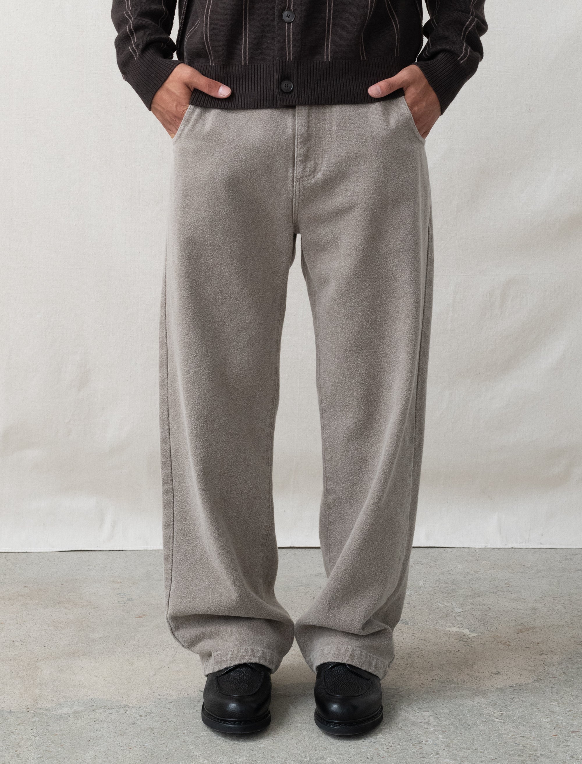 Person wearing gray pants and a black jacket against a plain background