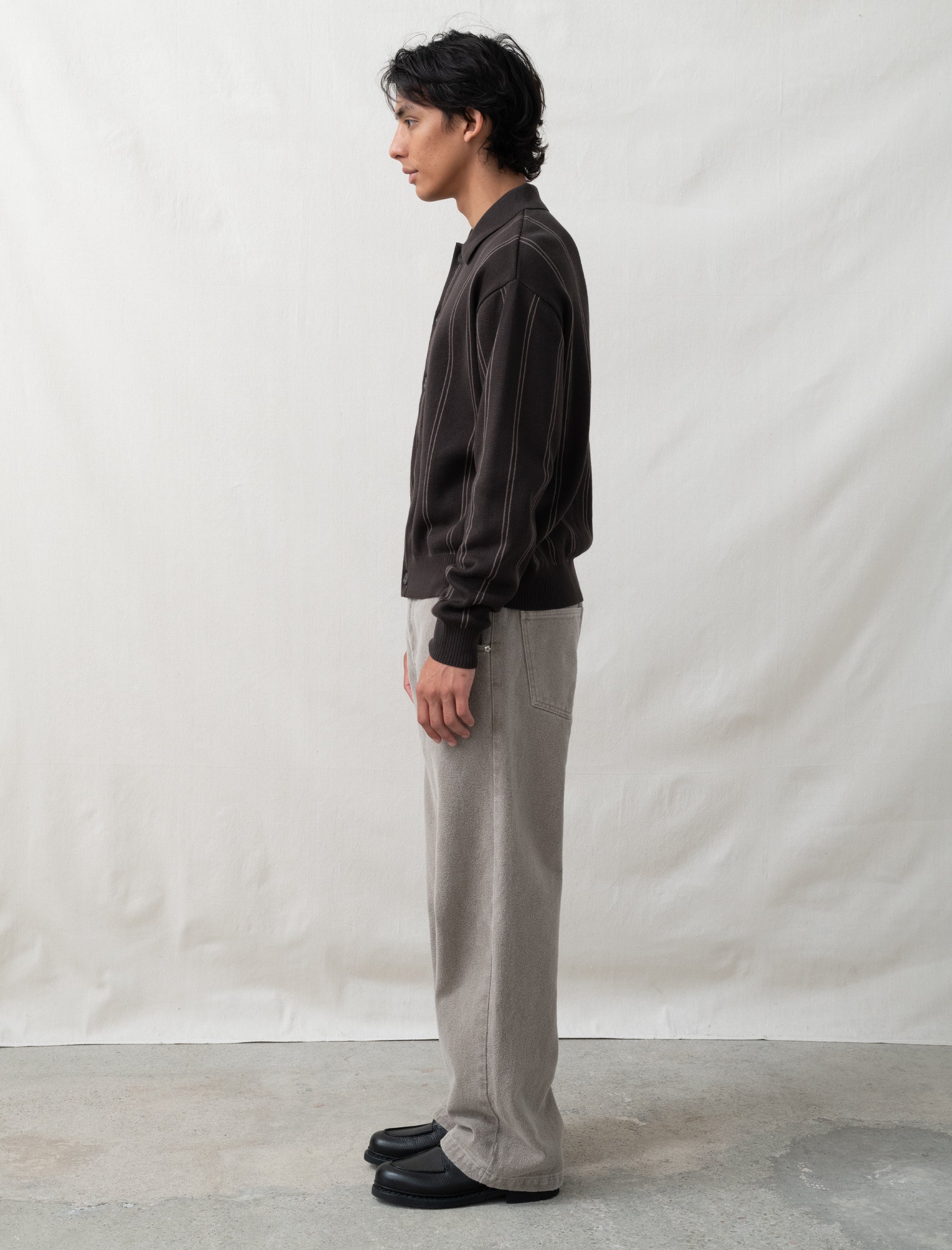 Person wearing a dark shirt and light pants standing against a plain white background