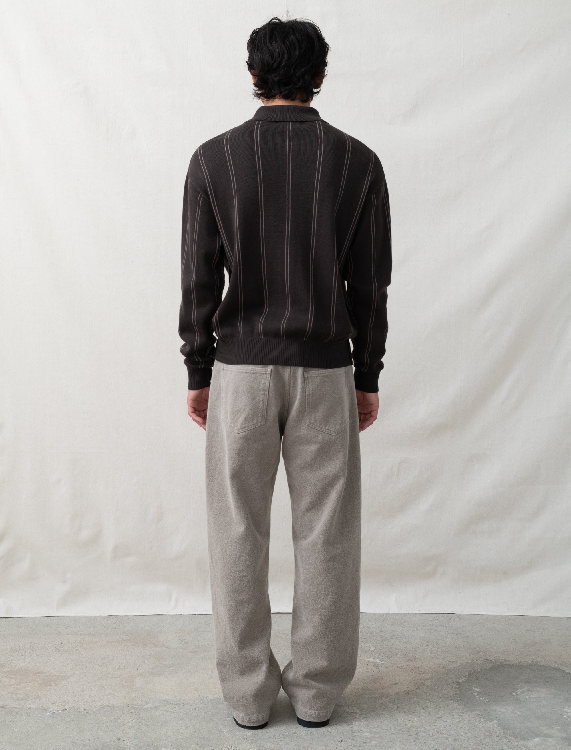 Person wearing a dark sweater and light gray pants against a plain white background