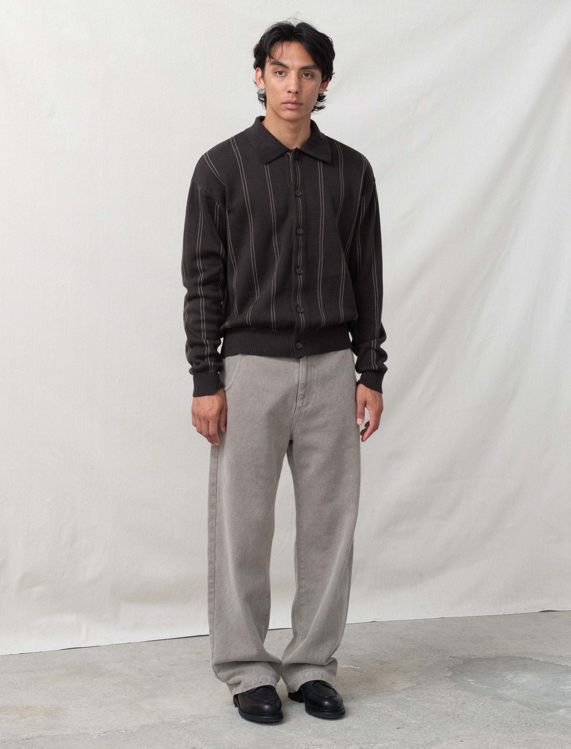 Man wearing a dark striped shirt and light gray pants against a white background