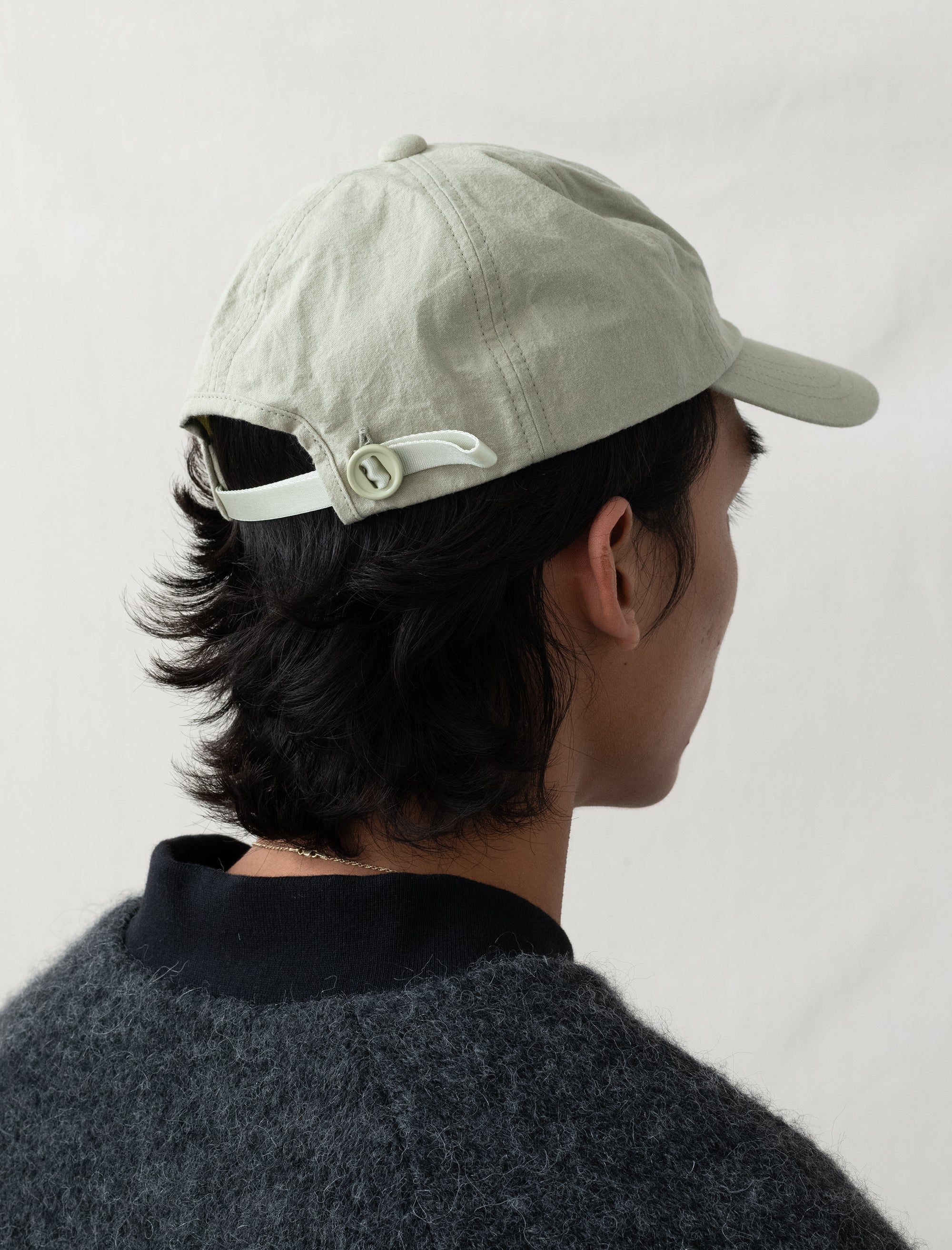 Person wearing a light-colored cap with a white strap on a plain background