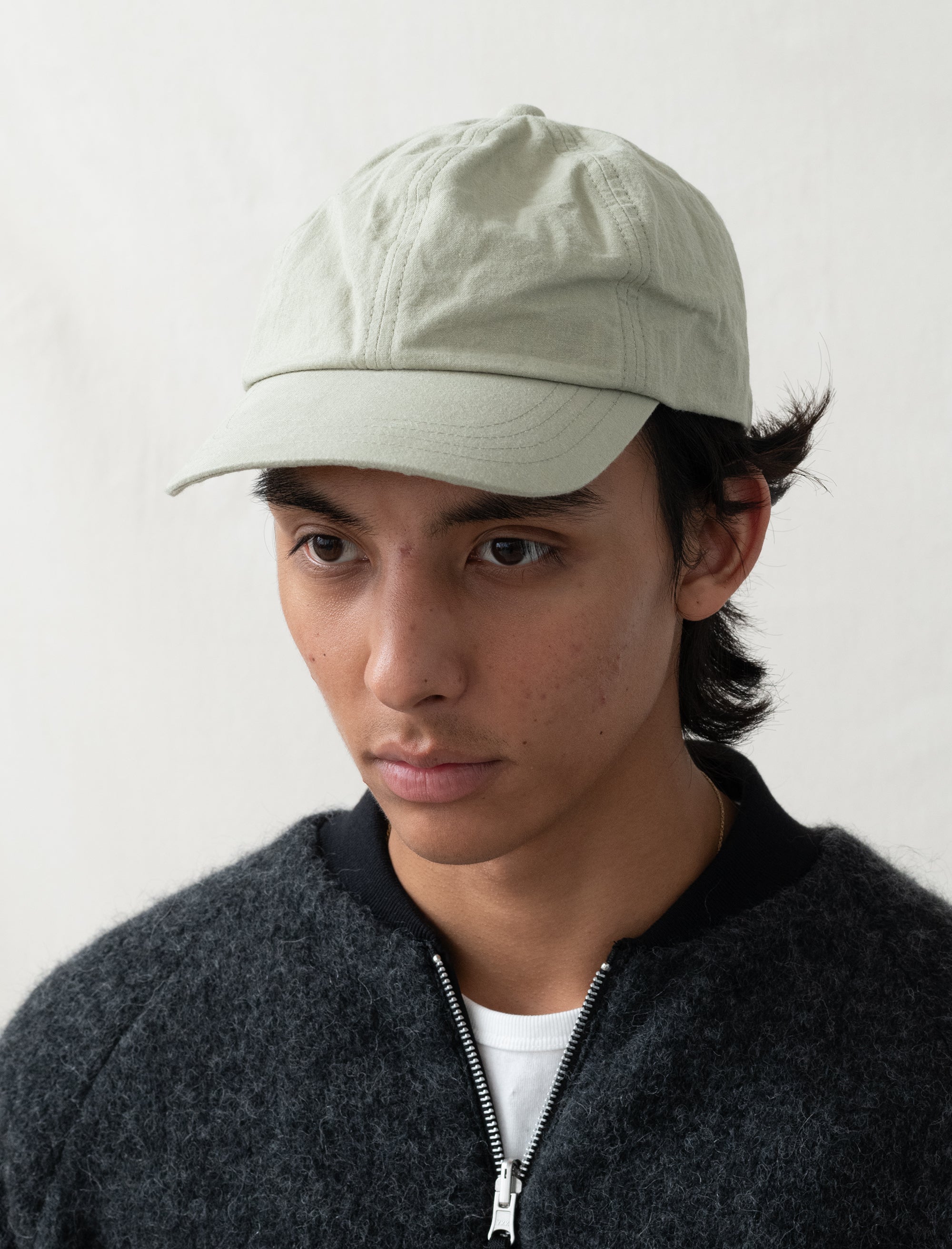 Person wearing a light-colored cap and dark jacket against a plain background