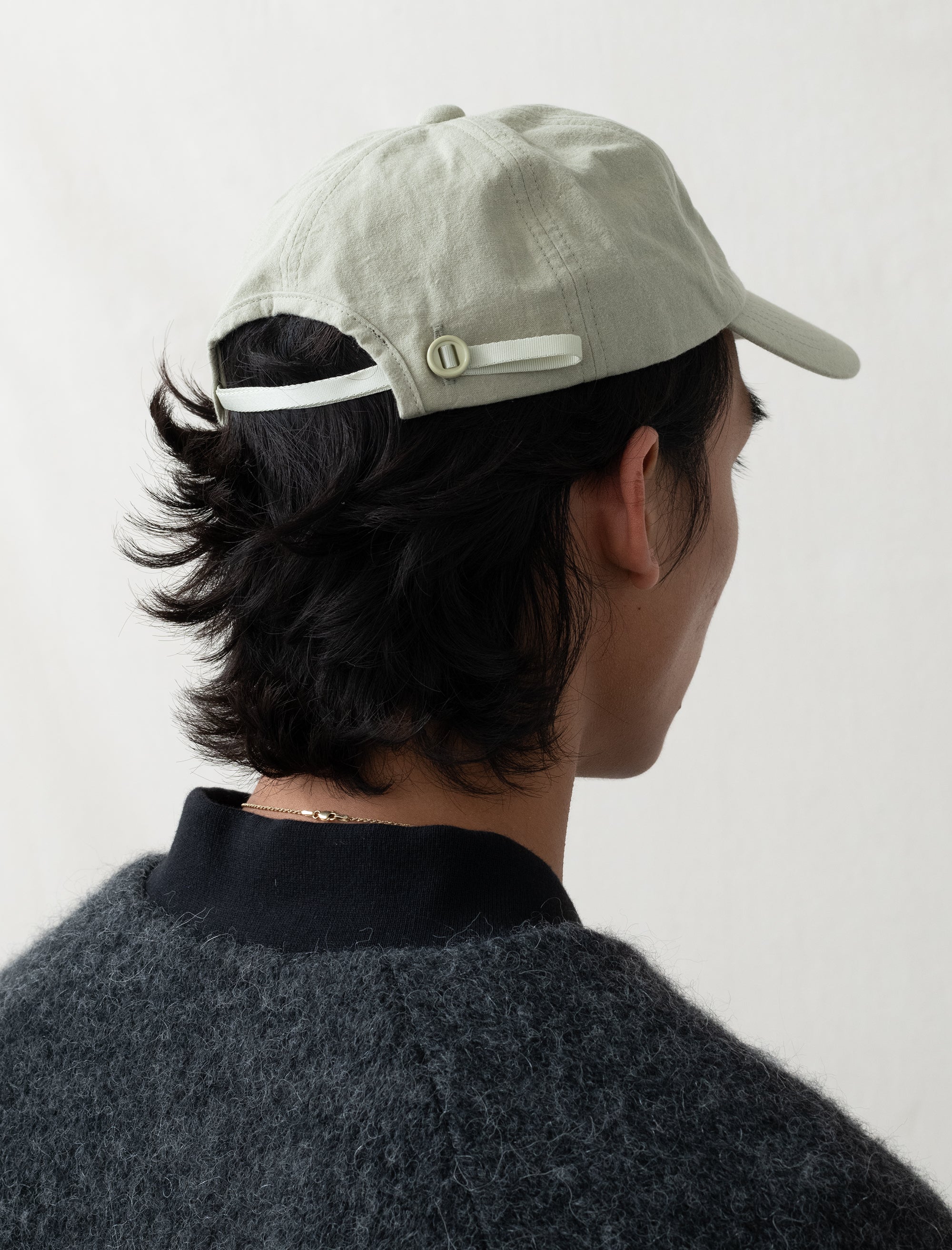 Person wearing a light gray cap with a button on a plain background