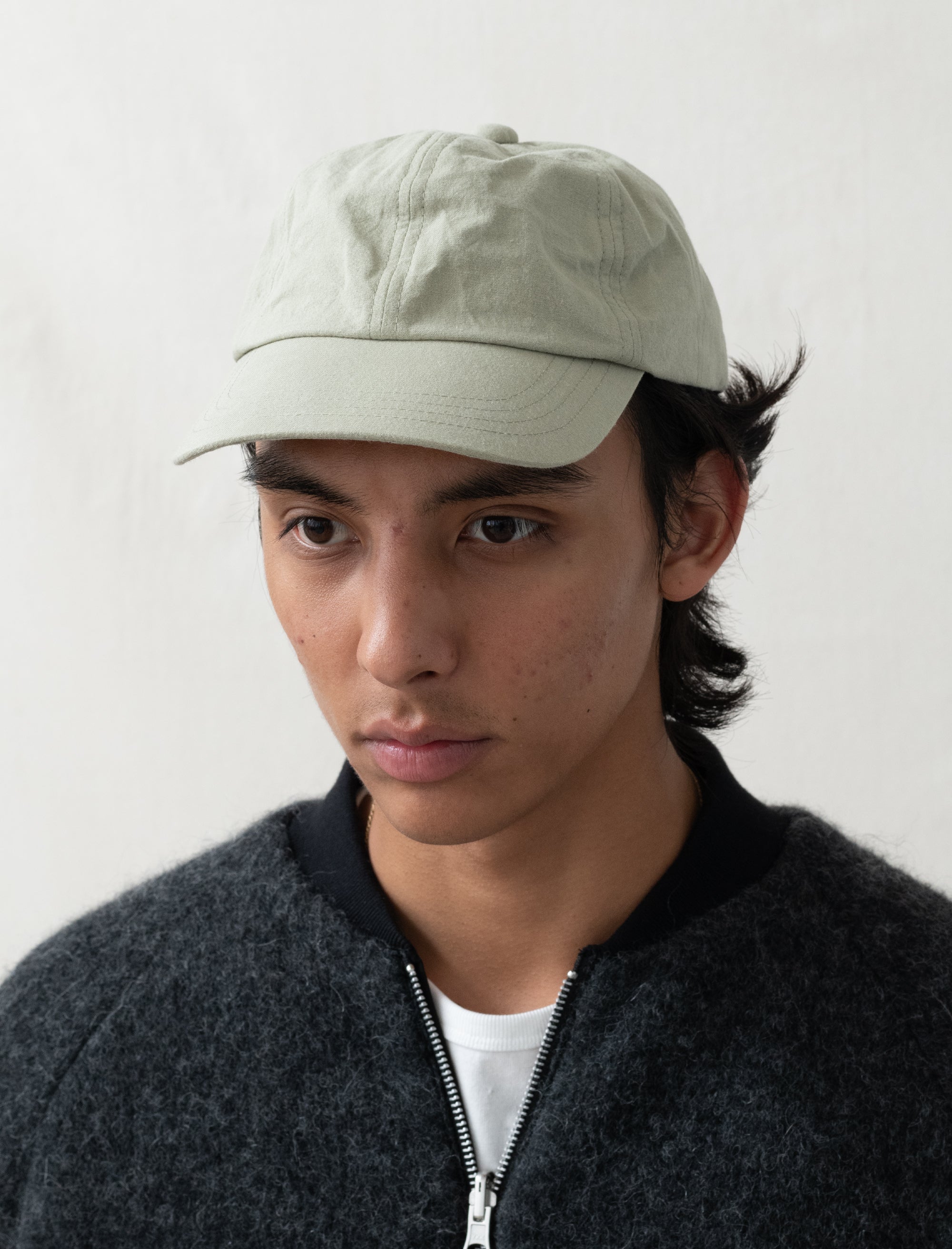 Person wearing a light-colored cap and dark jacket against a plain background