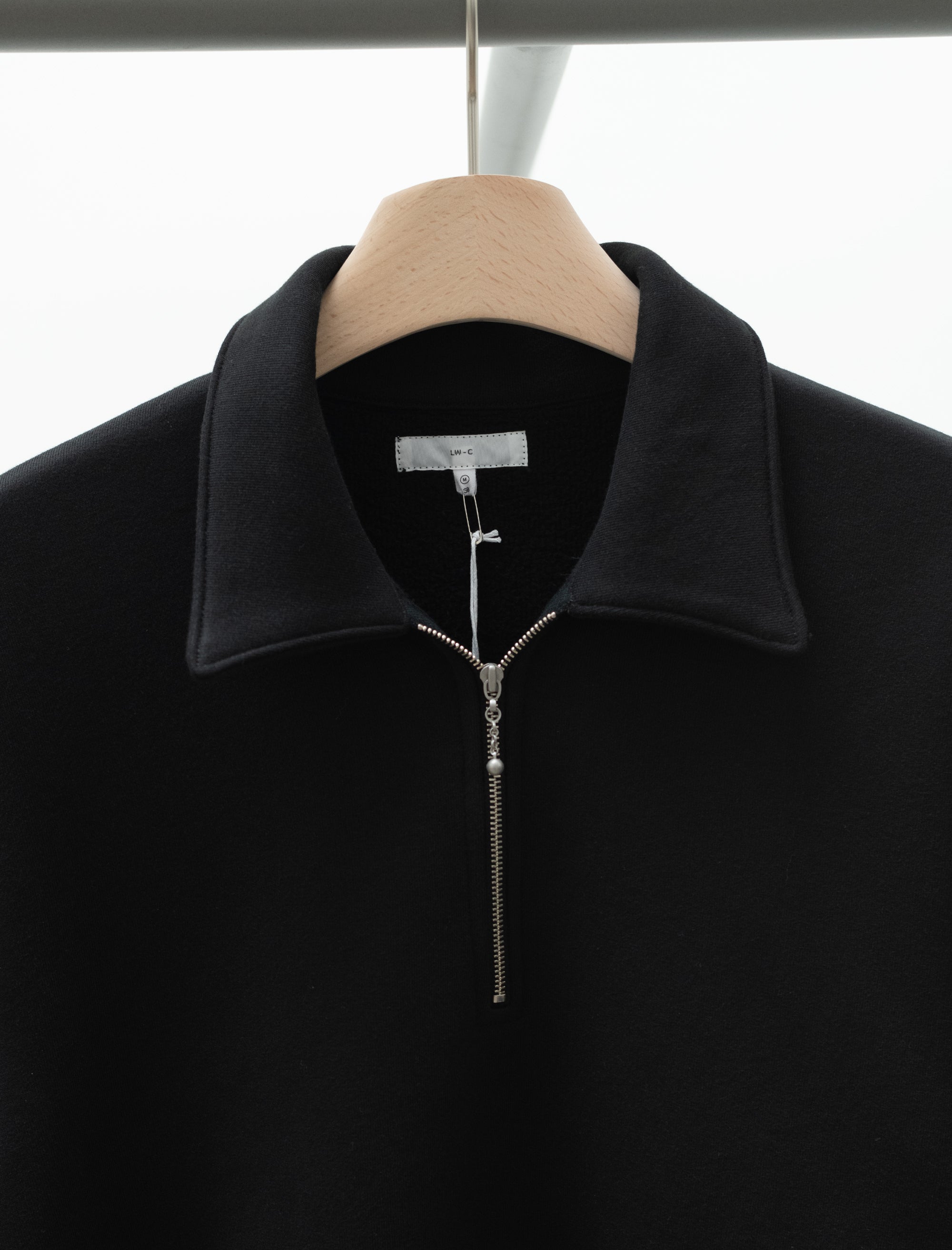 Black jacket with a zipper on a wooden hanger against a white background