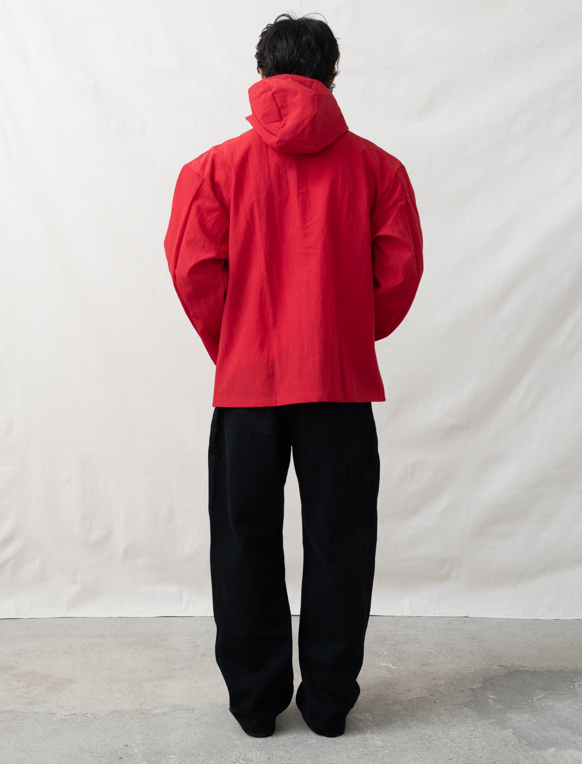 Person wearing a red raincoat and black pants standing against a white background