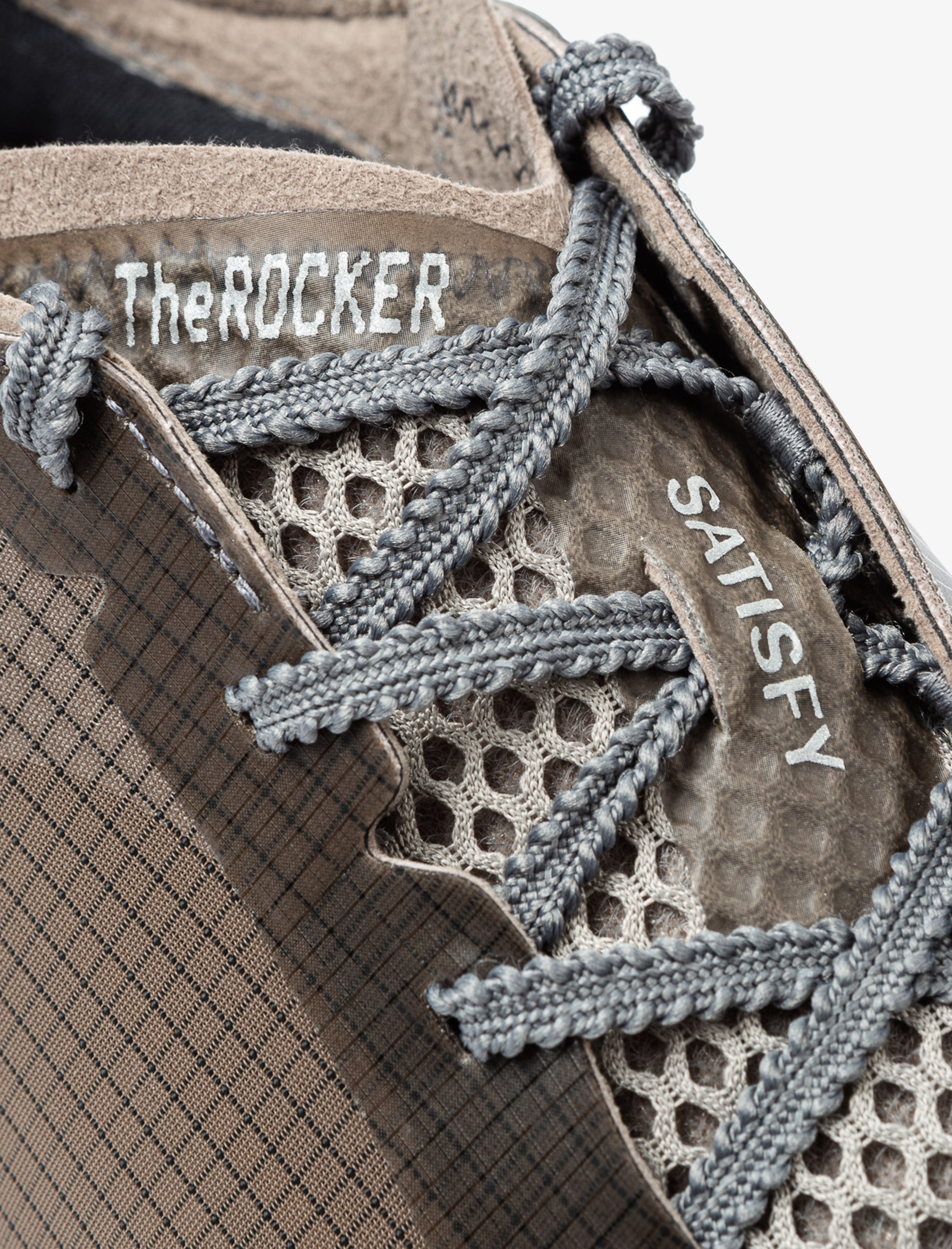 Close-up of a shoe with 'The Rocker' and 'Satisfy' branding on a textured background.