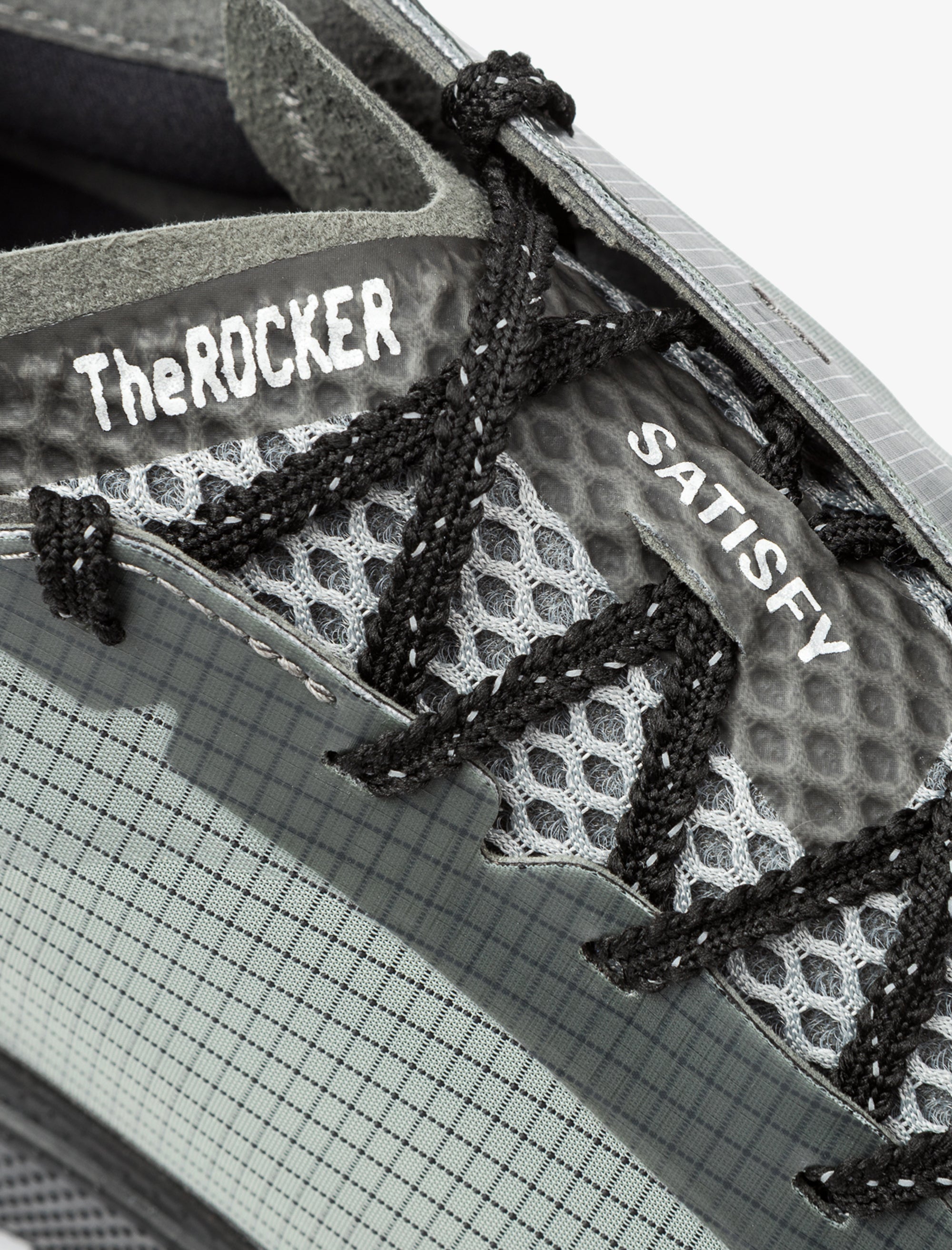 Close-up of a shoe with 'The Rocker' and 'Satisfy' branding on a grid background