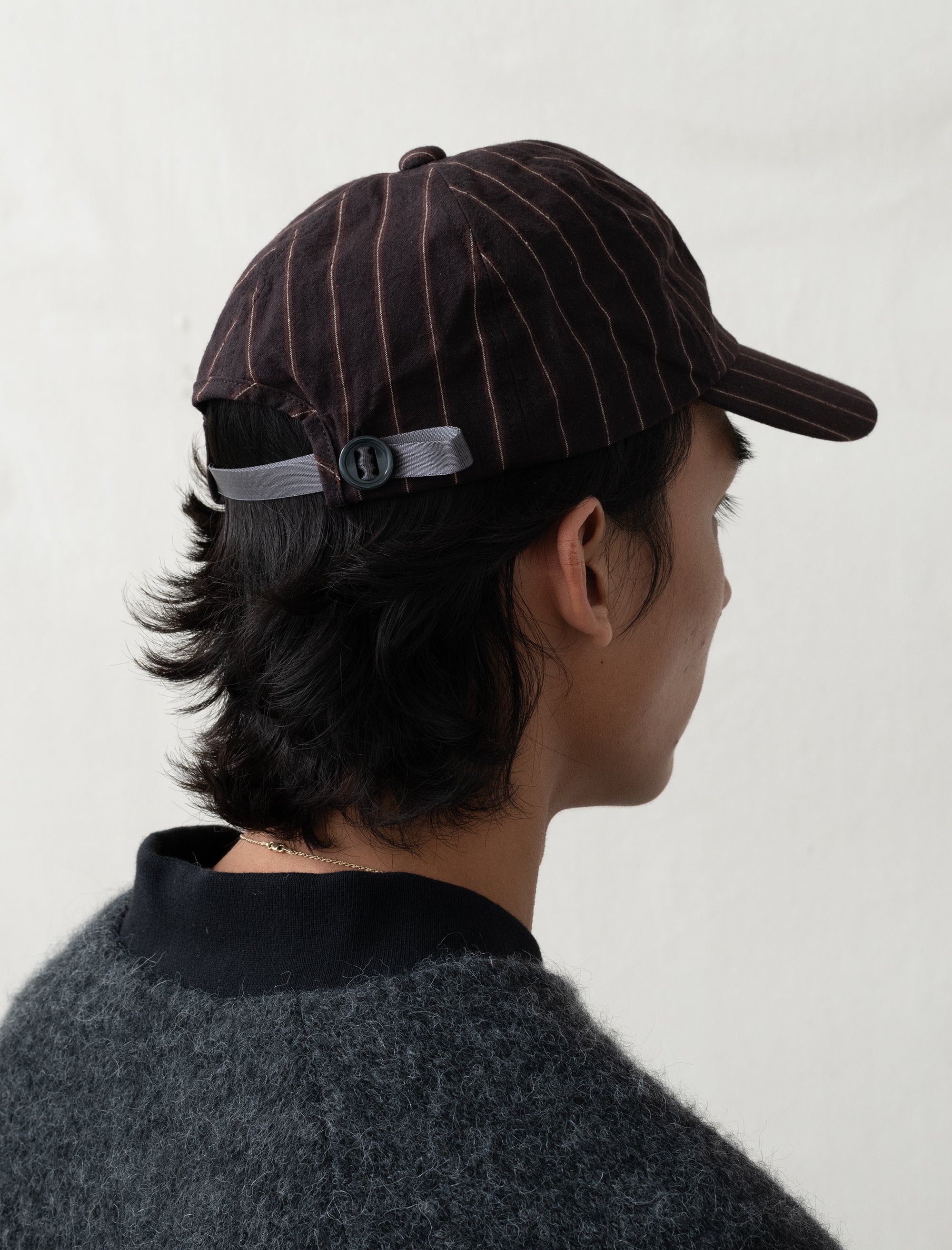 Person wearing a brown pinstripe cap with a white logo on a plain background