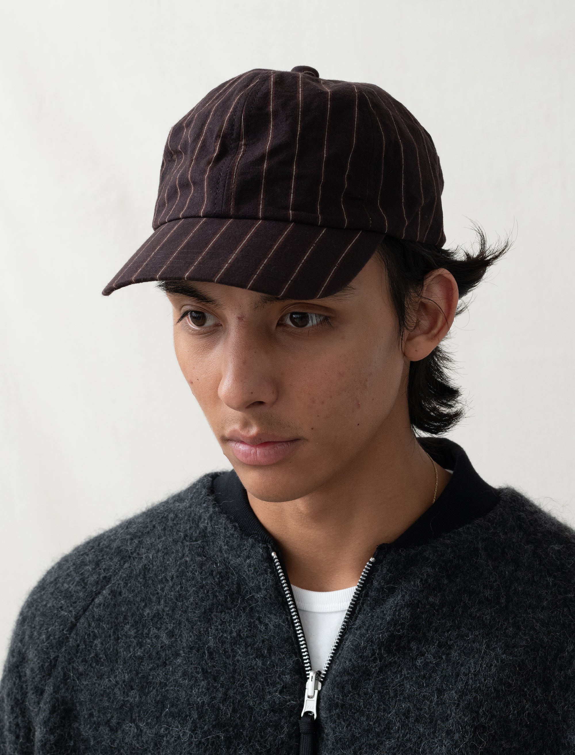 Person wearing a dark pinstripe cap and dark jacket against a white background