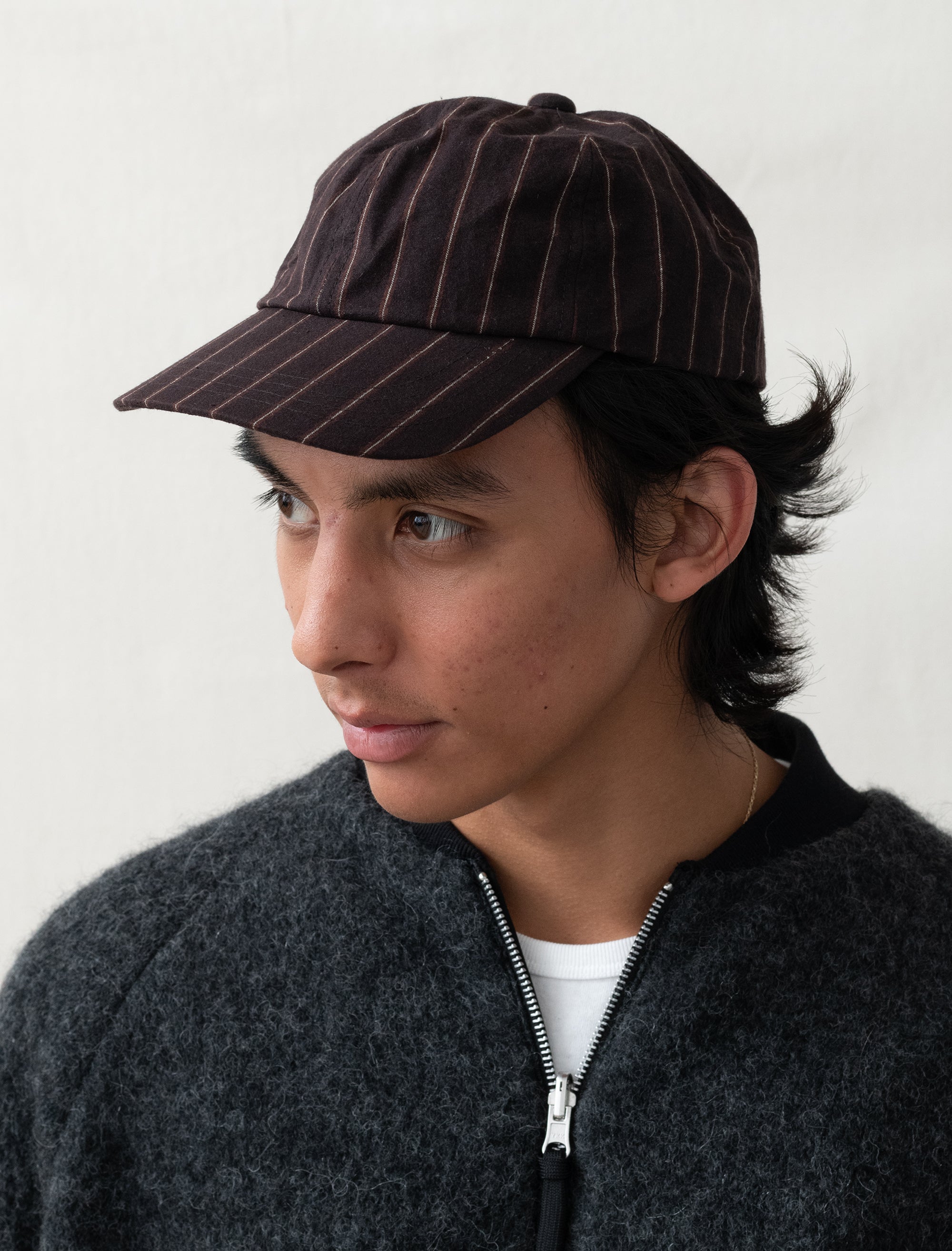 Person wearing a dark pinstripe cap and dark jacket against a white background