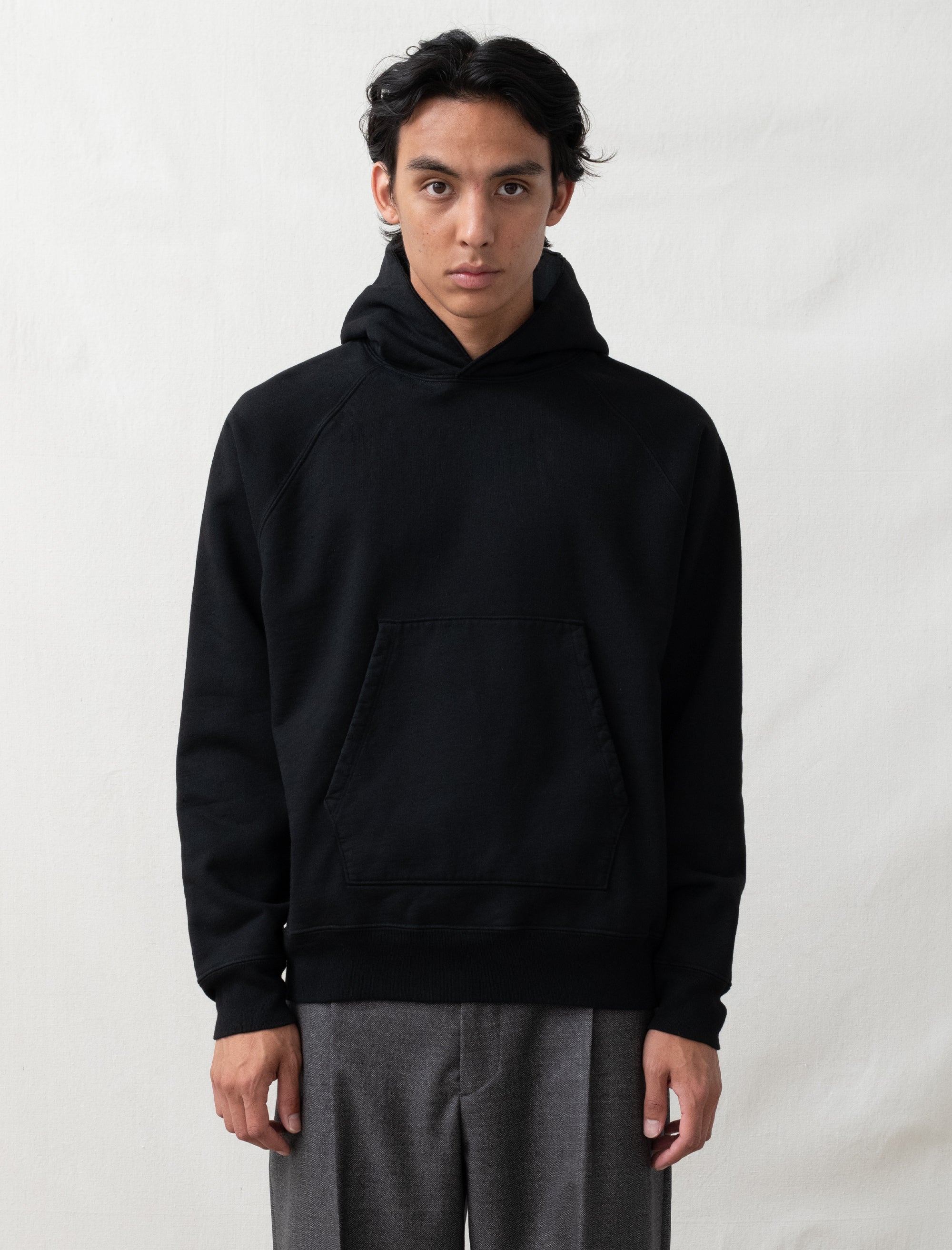 Person wearing a black hoodie and gray pants on a white background