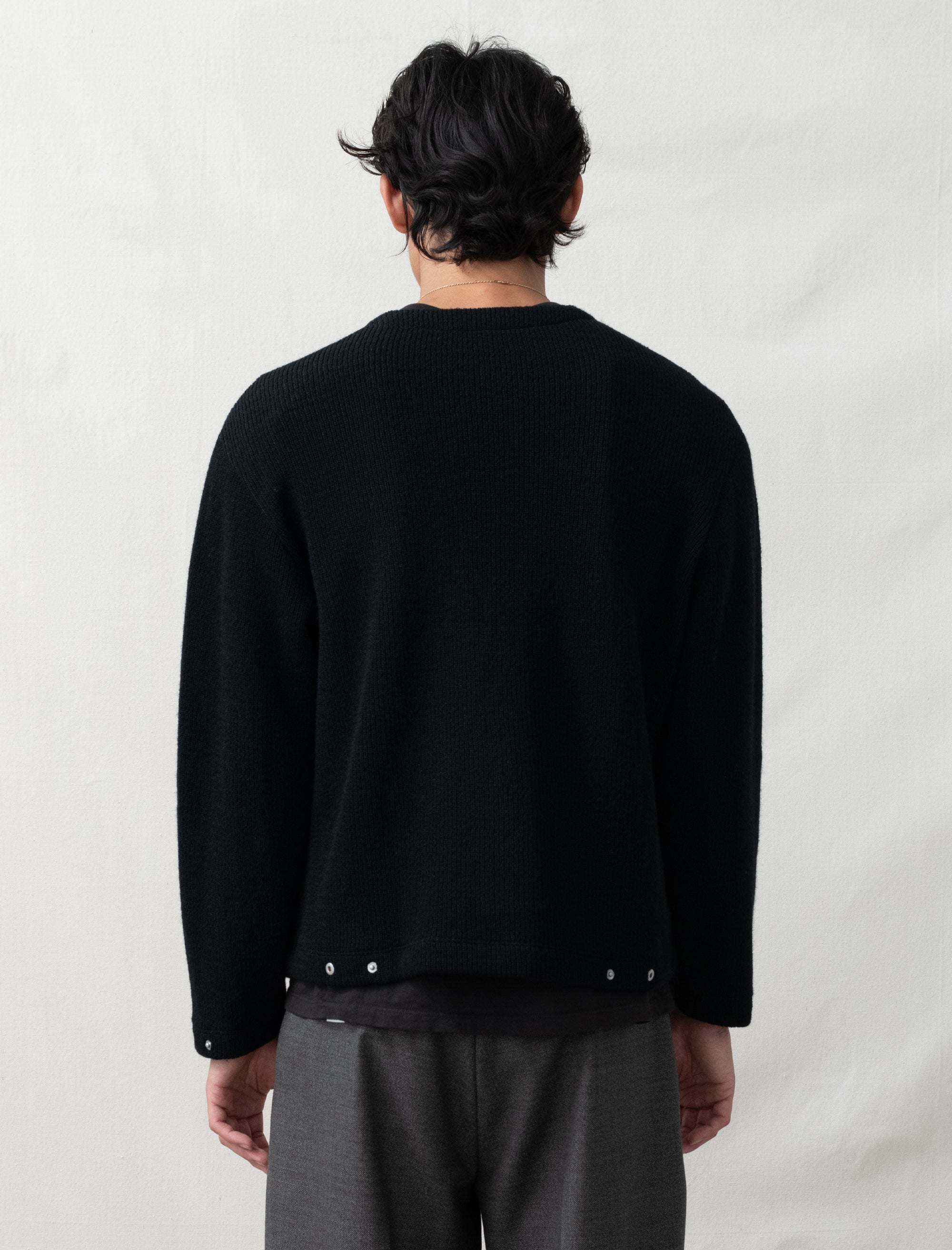 Person wearing a black sweater with white buttons on a plain background