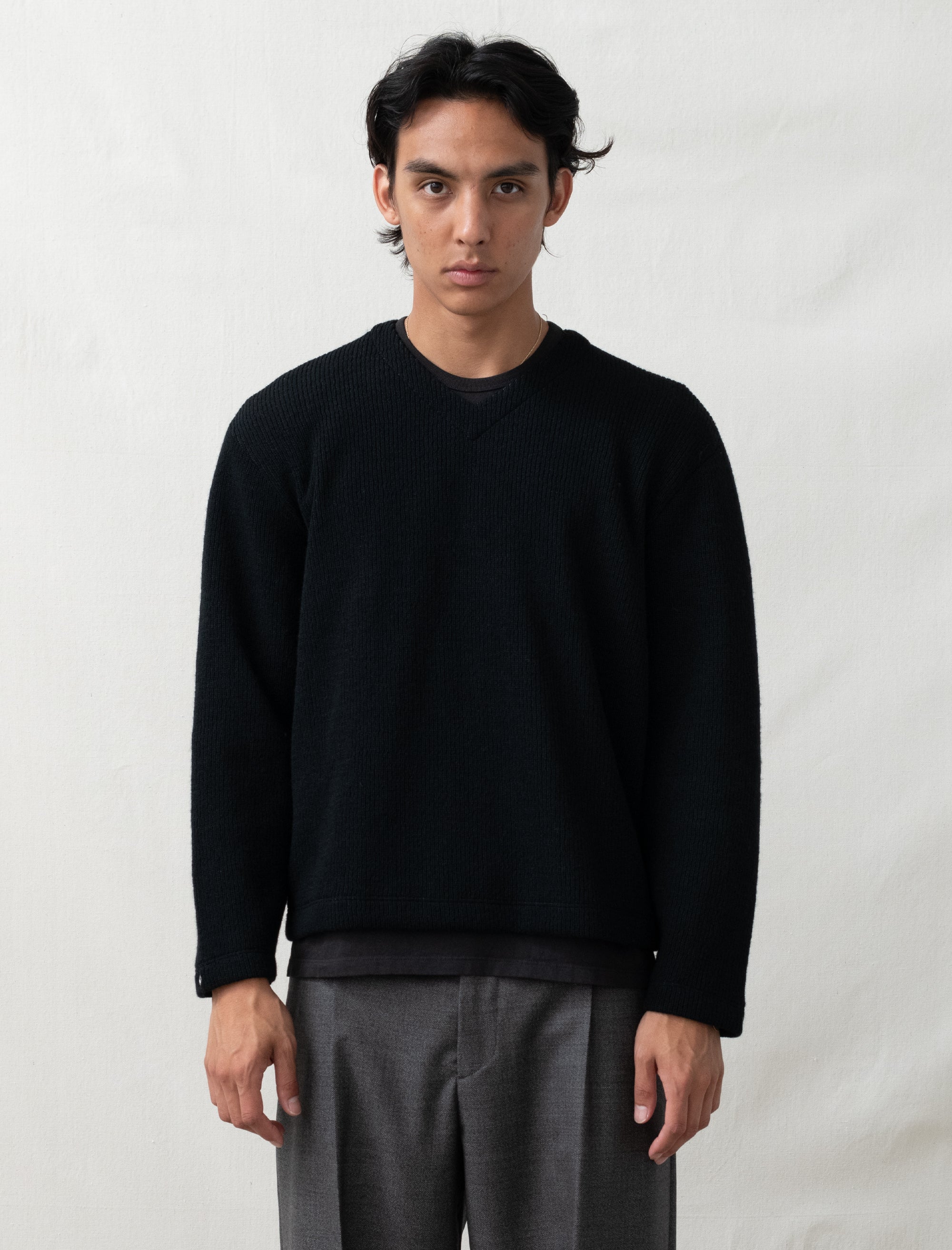 Person wearing a black sweater and gray pants against a white background