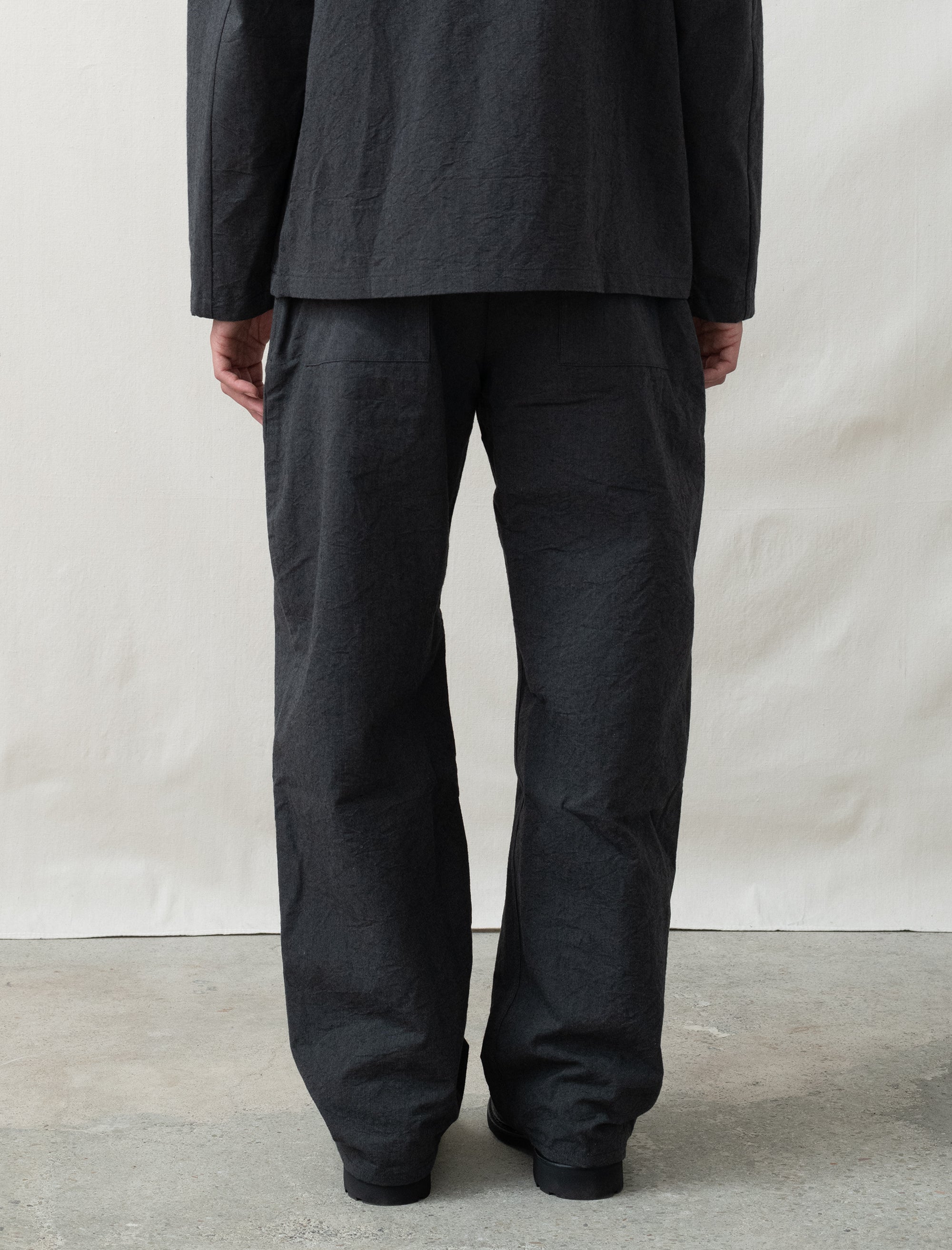 Person wearing black pants and a dark jacket against a plain background