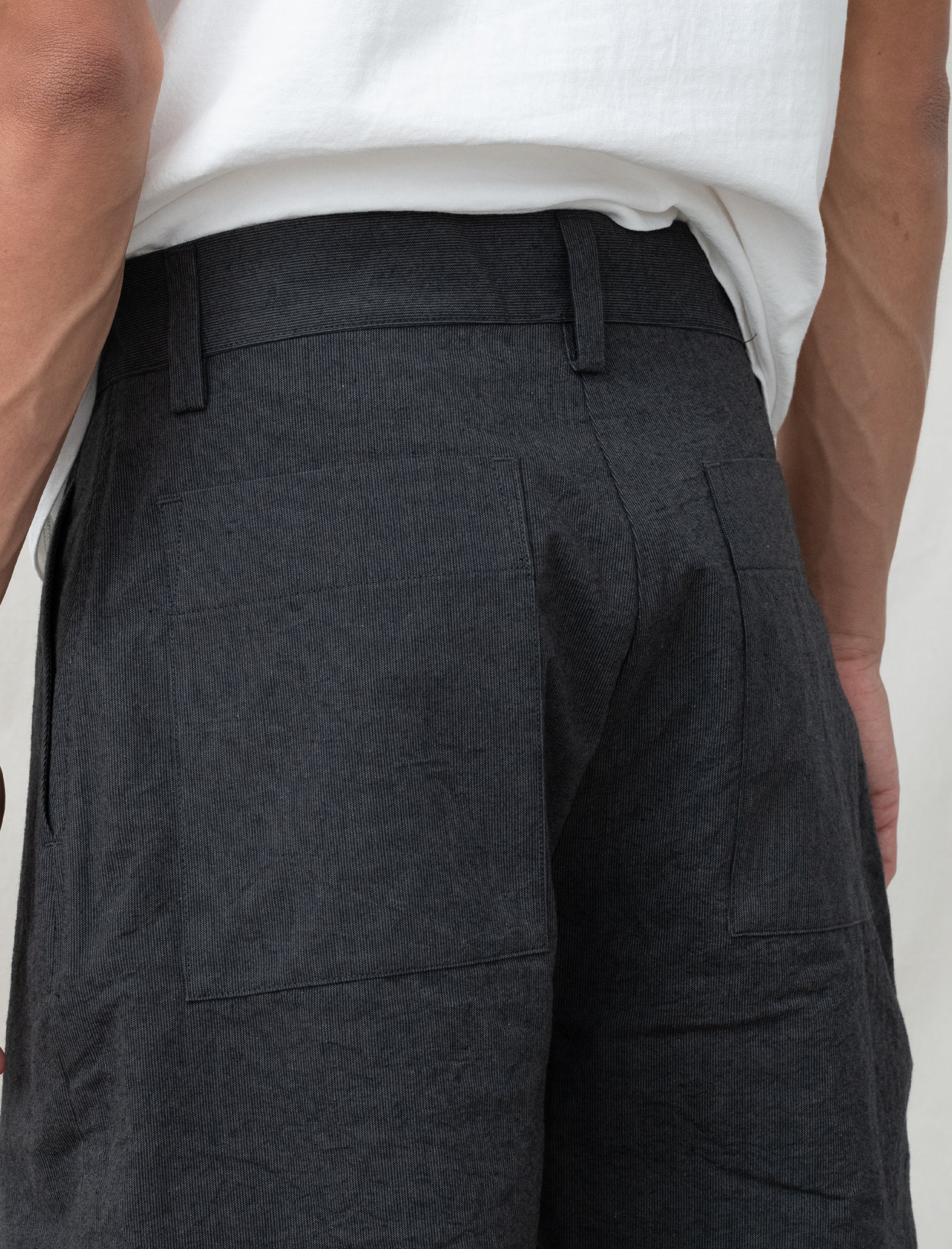 Person wearing dark gray pants with a white shirt underneath on a plain background